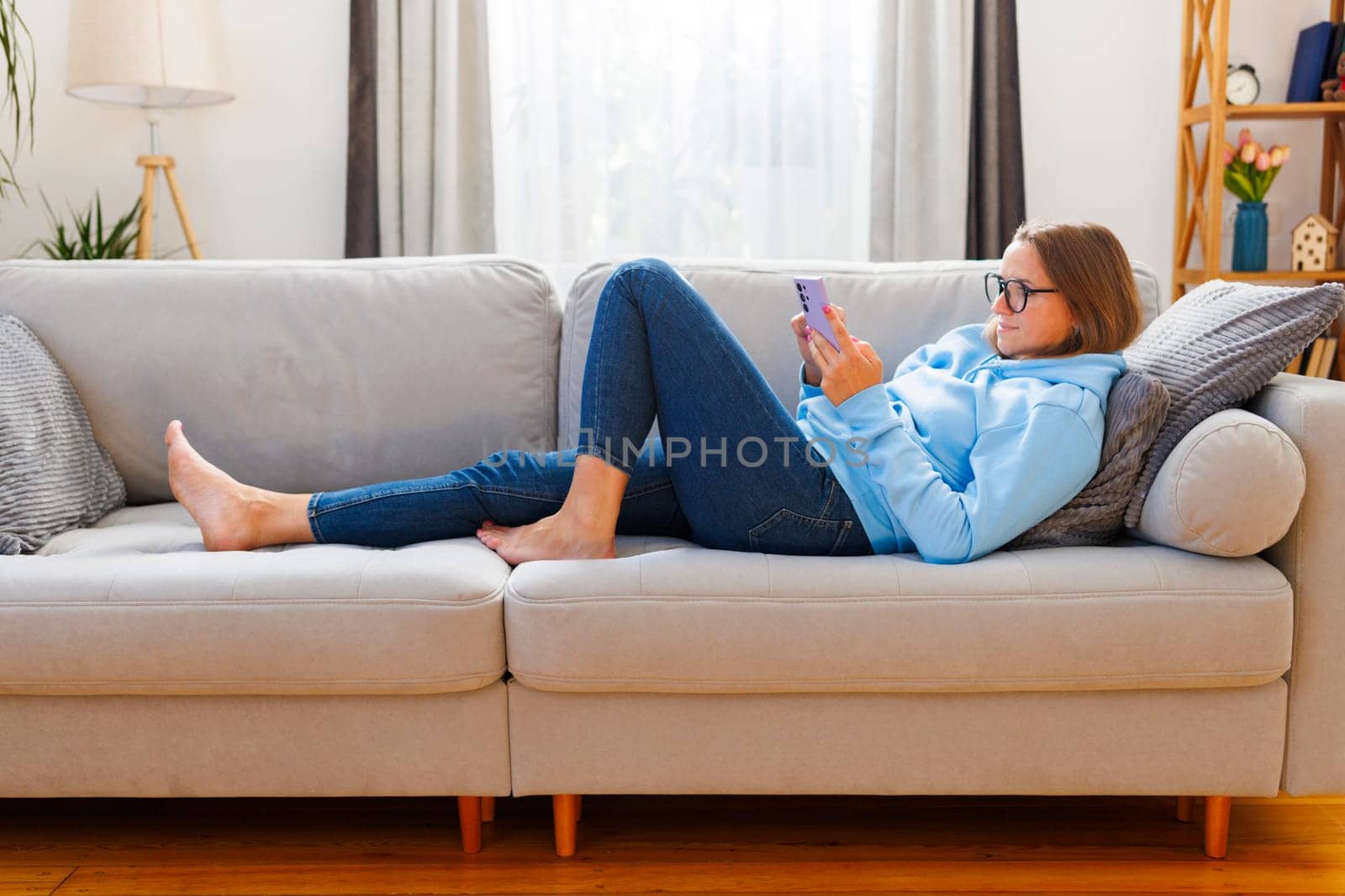 Relaxed woman lounging on a sofa with a smartphone. Casual indoor living space with copy space for design and print