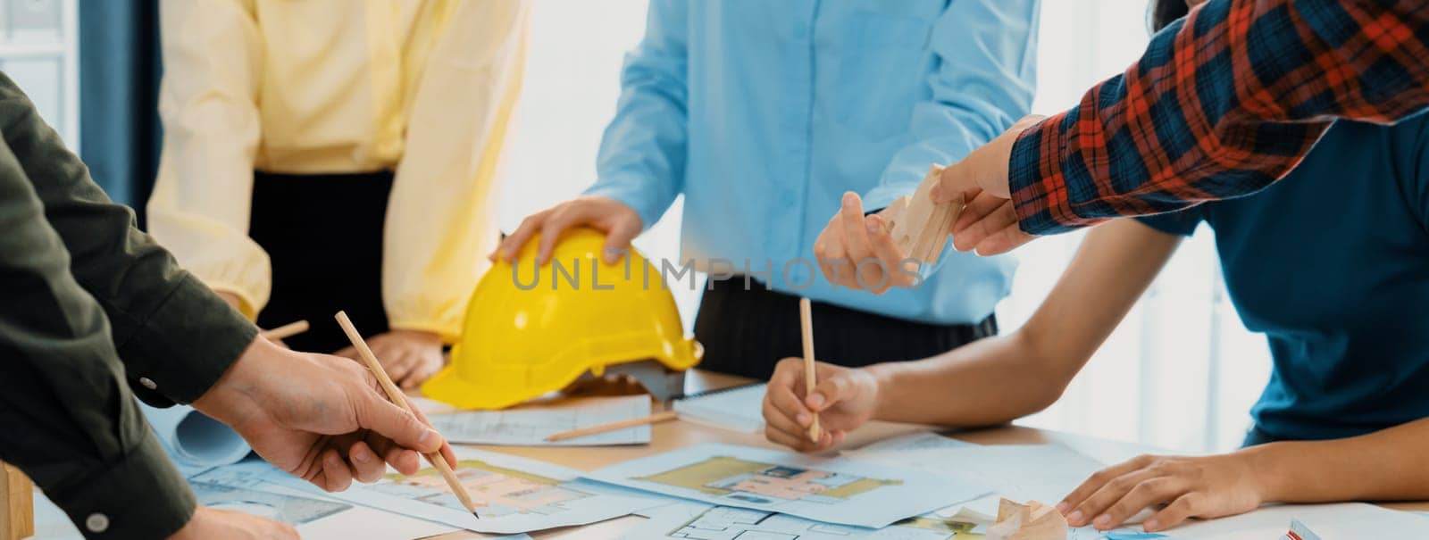 Professional architect team and safety engineer with safety helmet brainstorming about architectural project on meeting table with blueprint scatter around. Close up. Focus on hand. Delineation.