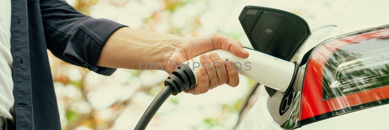 Panorama banner man recharging battery for electric car during autumnal road trip travel EV car in autumnal forest. Eco friendly travel on vacation during autumn with electric vehicle. Exalt
