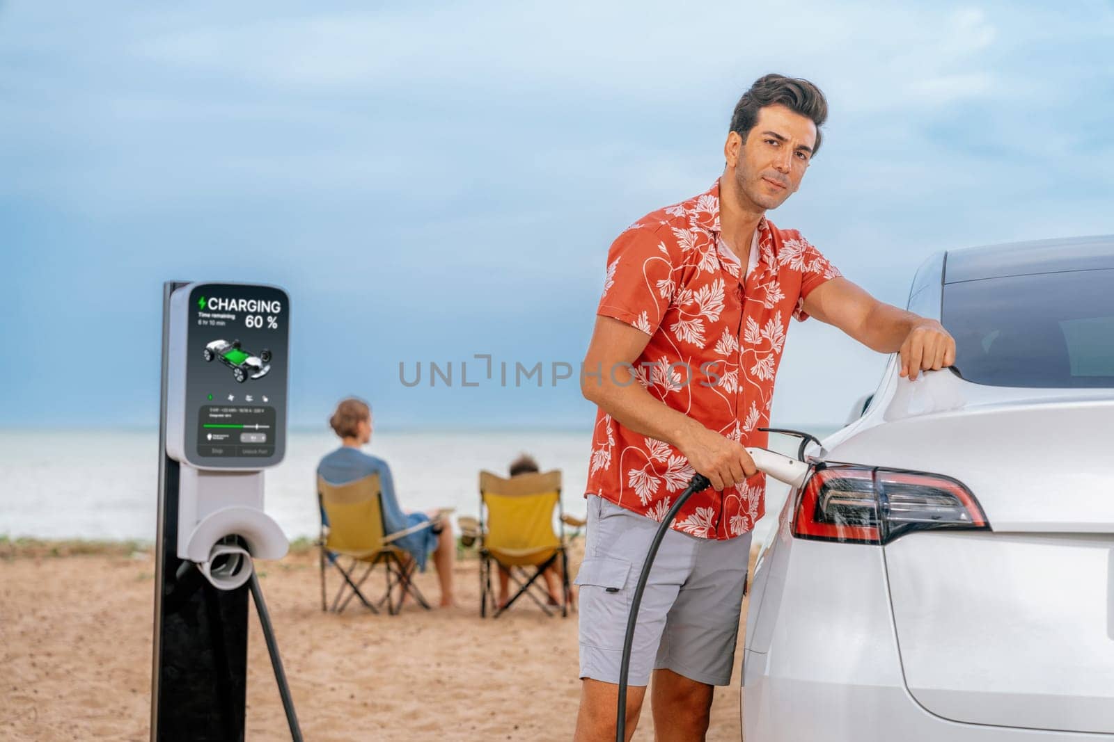 Family vacation trip traveling by the beach with electric car, dad or father recharge EV car while his family enjoy seascape beach. Family trip with alternative energy and eco-friendly car. Perpetual