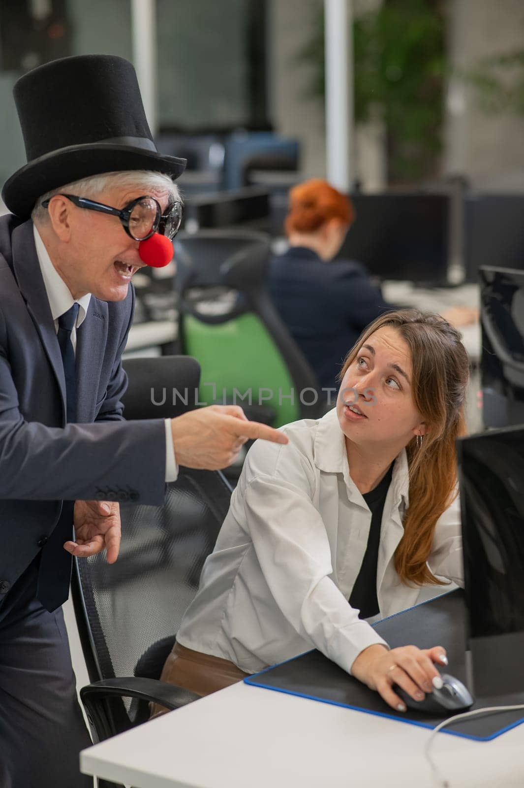 Caucasian woman communicates with an elderly man in a clown costume in the office. Vertical photo. by mrwed54