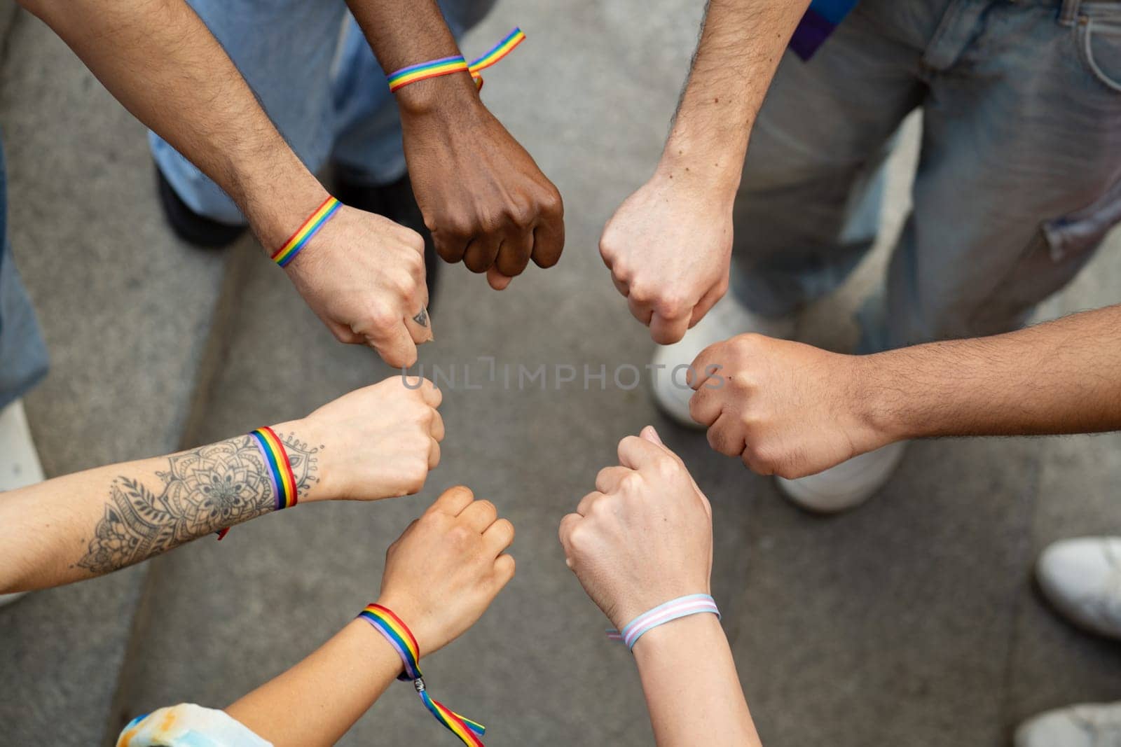 A group of people with rainbow bracelets on their wrists are holding hands in a circle. Concept of unity and support for the LGBTQ community