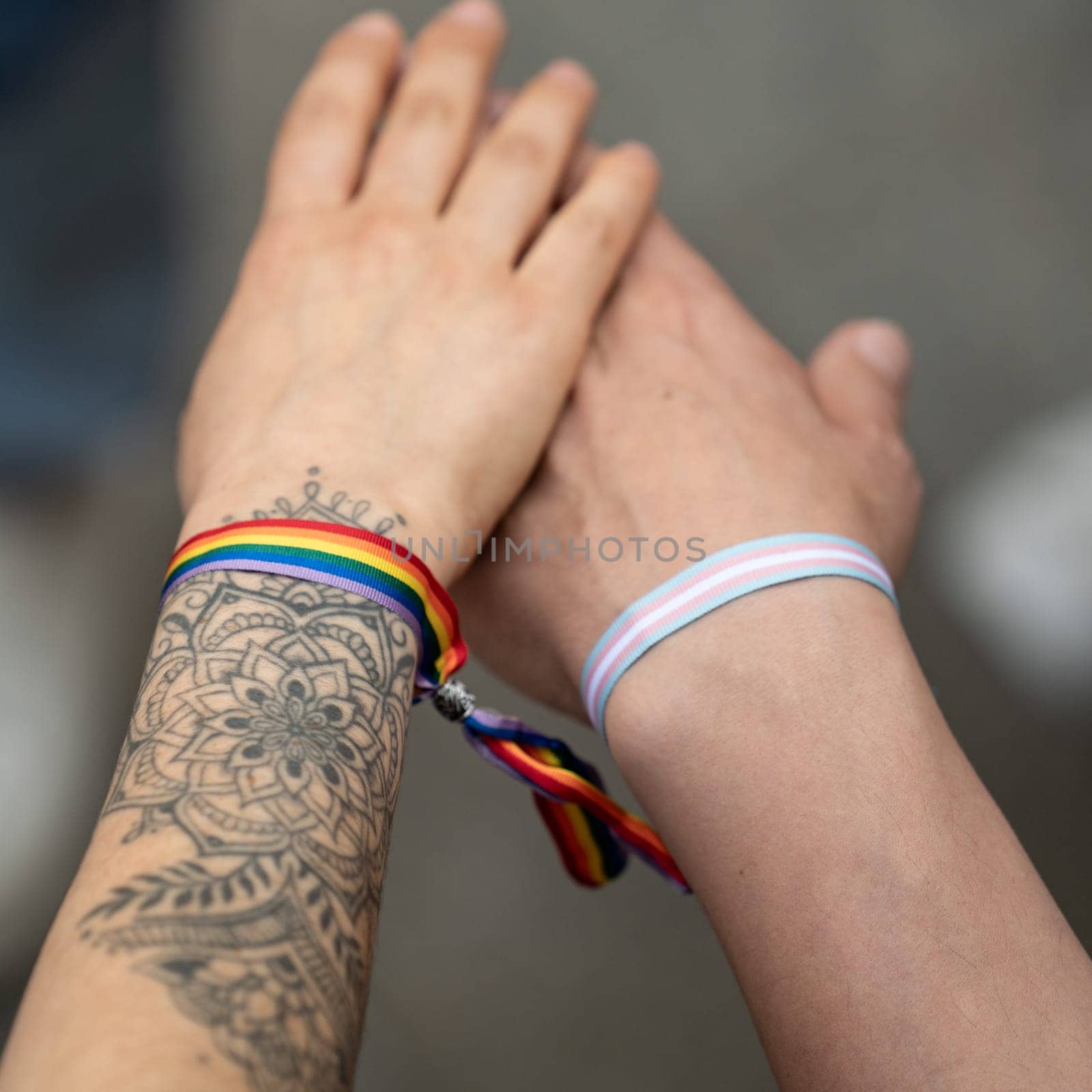 Hands of lesbian women with a ribbon of LGBT rainbow colors tied together. LGBT pride concept, lgbt rights campaign by papatonic