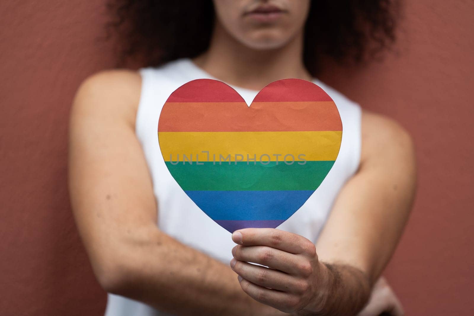Close-up of man holding a paper heart LGBT flag colors. Gay love concept.