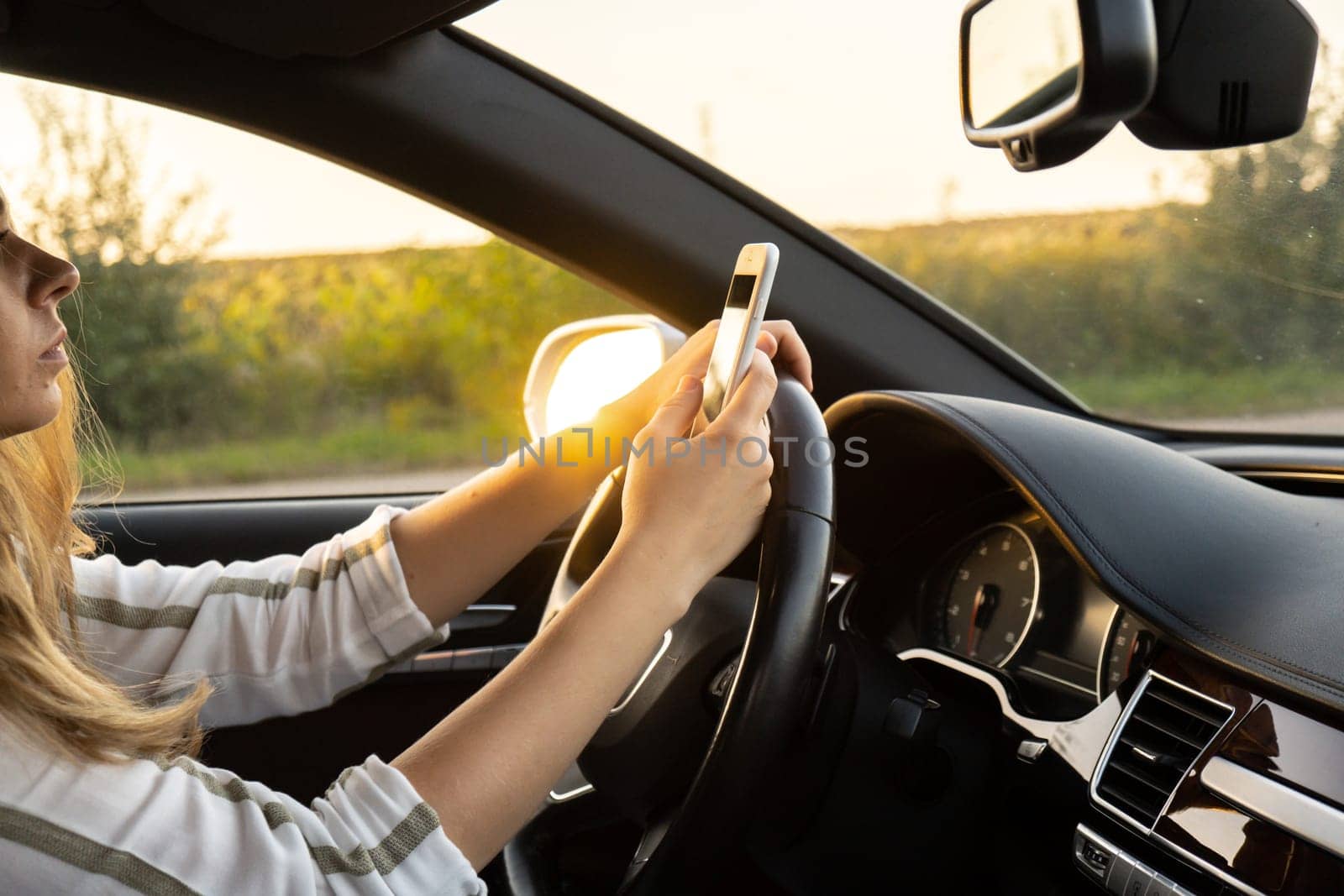 Woman sending messages with smartphone while driving automobile. Female driver using mobile phone on the road during driving the car. Safety and technology concept