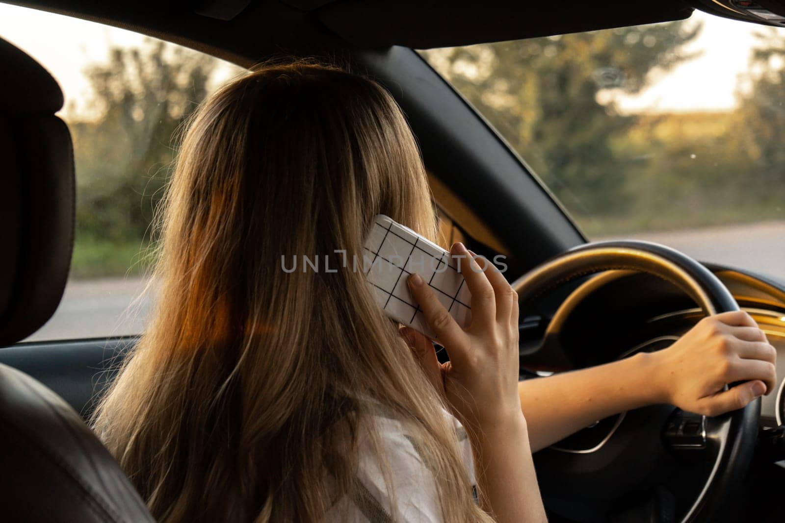 Happy young woman speaking by mobile phone while driving car. Business woman talking phone call in automobile. Unsafely risky driving multitasking by anna_stasiia