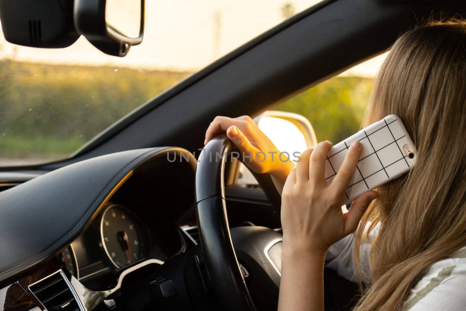 Happy young woman speaking by mobile phone while driving car. Business woman talking phone call in automobile. Unsafely risky driving. Concept of multitasking