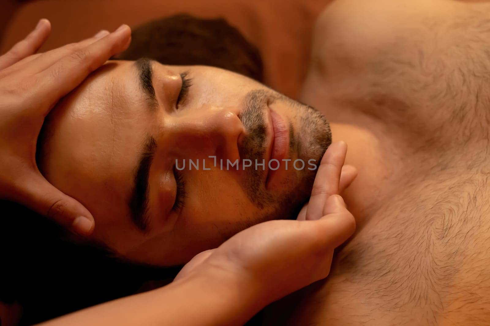 Caucasian man enjoying relaxing anti-stress head massage and pampering facial beauty skin recreation leisure in warm candle lighting ambient salon spa in luxury resort or hotel. Quiescent