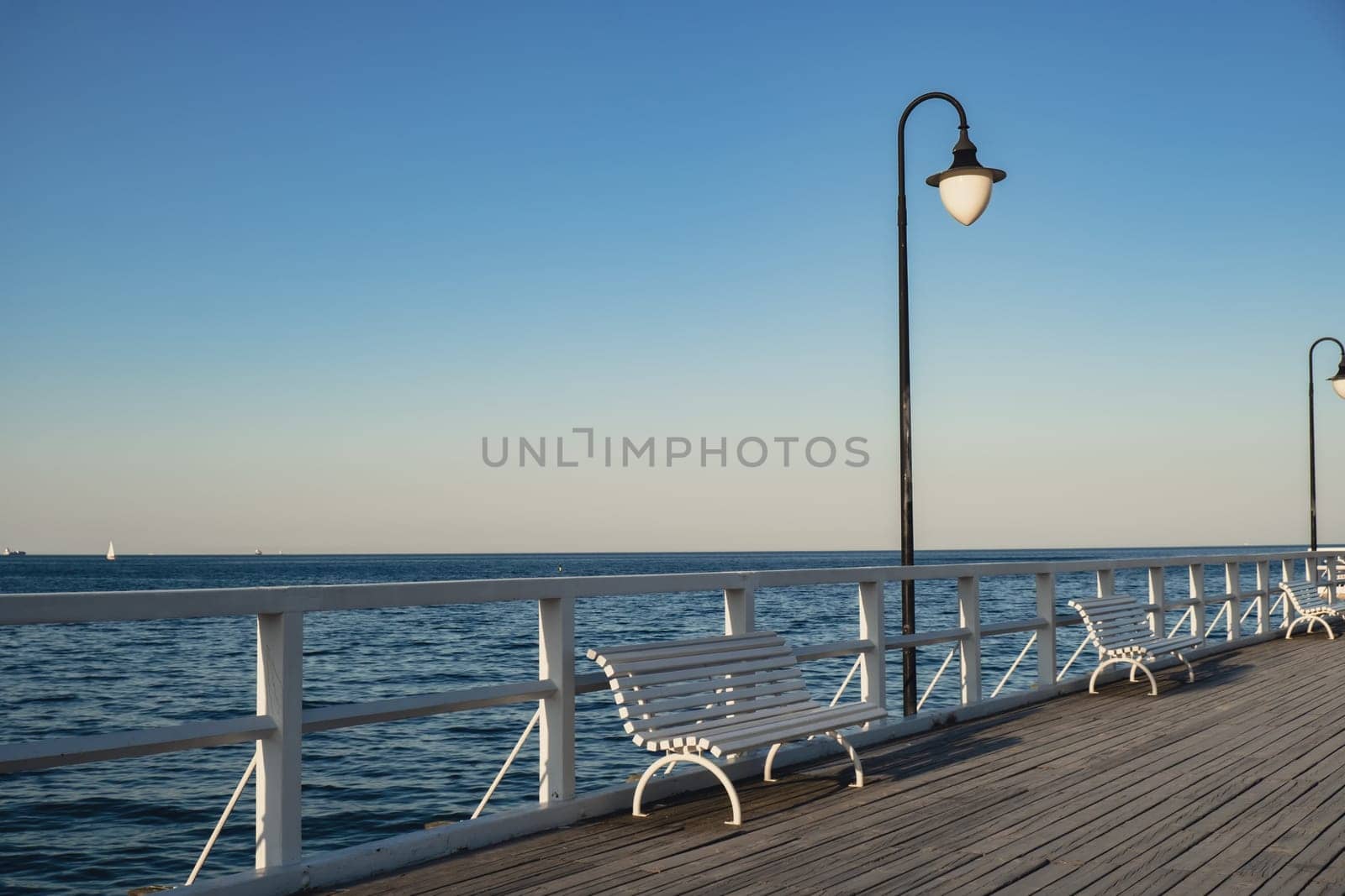 White Old wood bridge pier against beautiful sunset sky natural background, backdrop wallpaper multipurpose sea scene. White benches no people in Gdynia Orlowo, Poland. Wooden pier, molo with marina and beach by anna_stasiia