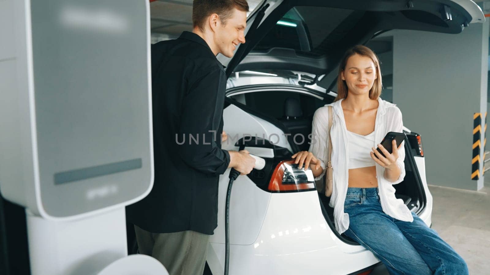 Electric car driver checks battery charging status app screen in car innards by biancoblue