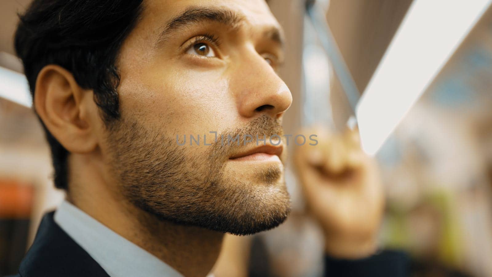 Closeup image of handsome caucasian business man standing in train while wearing suit. Professional project manager traveling by train or public transport surrounded by passenger or people. Exultant.