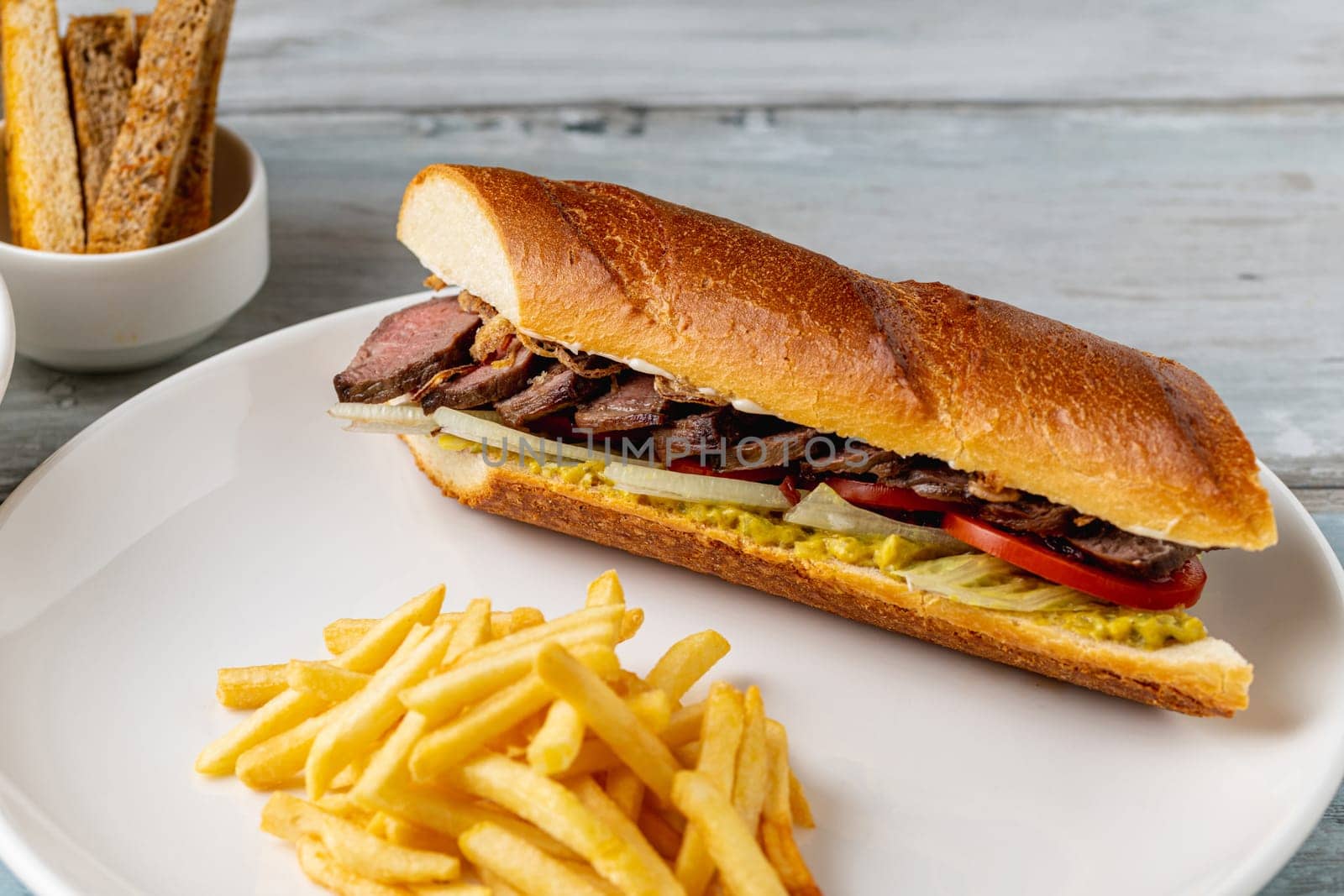 Grilled steak sandwich with french fries on a white porcelain plate by Sonat
