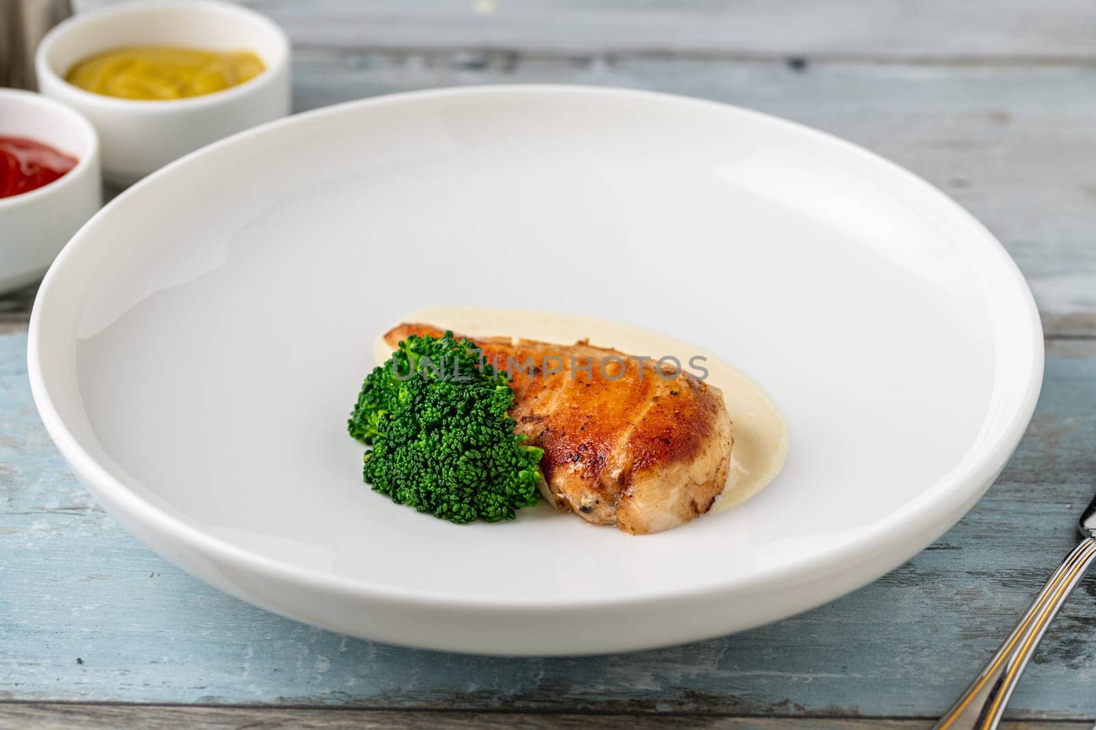 Grilled chicken breast with broccoli and sauce on a white porcelain plate