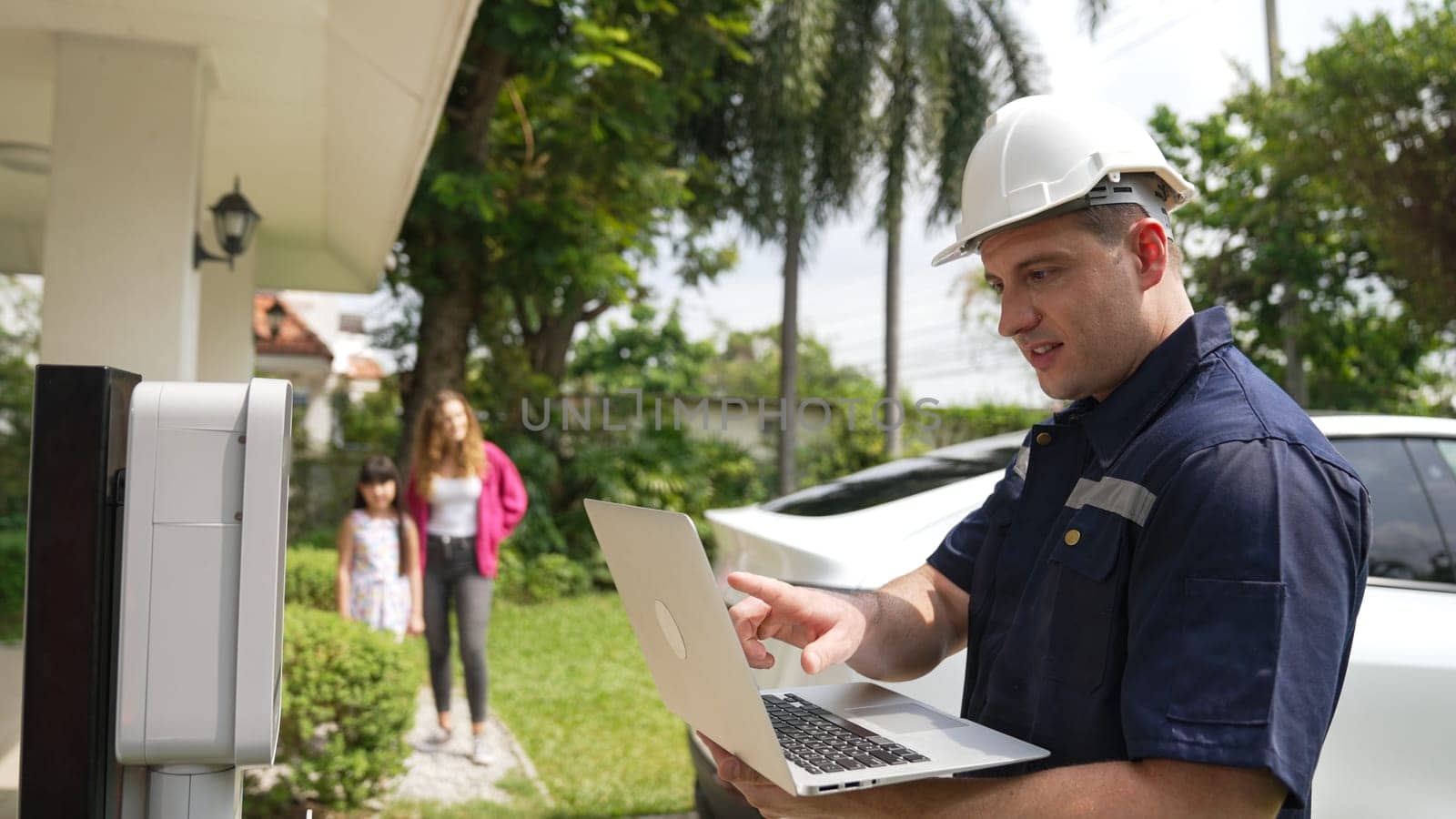 Qualified technician working on home EV charging station installation, making troubleshooting and configuration setup on charging system with laptop for EV at home. Synchronos