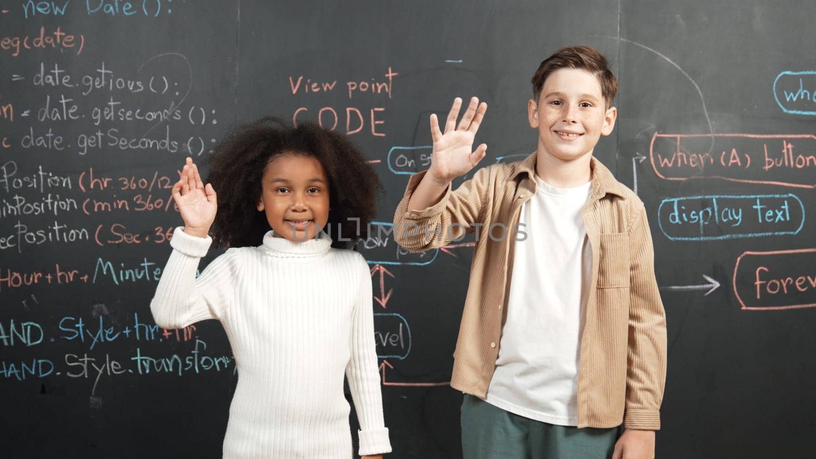 Panorama shot of diverse student smiling and waving hand at blackboard with engineering code or prompt written. Smart children looking at camera and greeting while study in STEM classroom. Erudition.