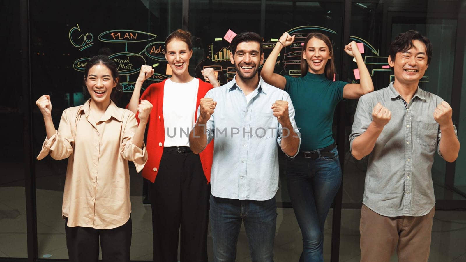 Group of businesspeople applause to celebrate successful project while looking at camera. Professional diverse business team standing at glass wall with marketing strategy, idea,plan. Tracery