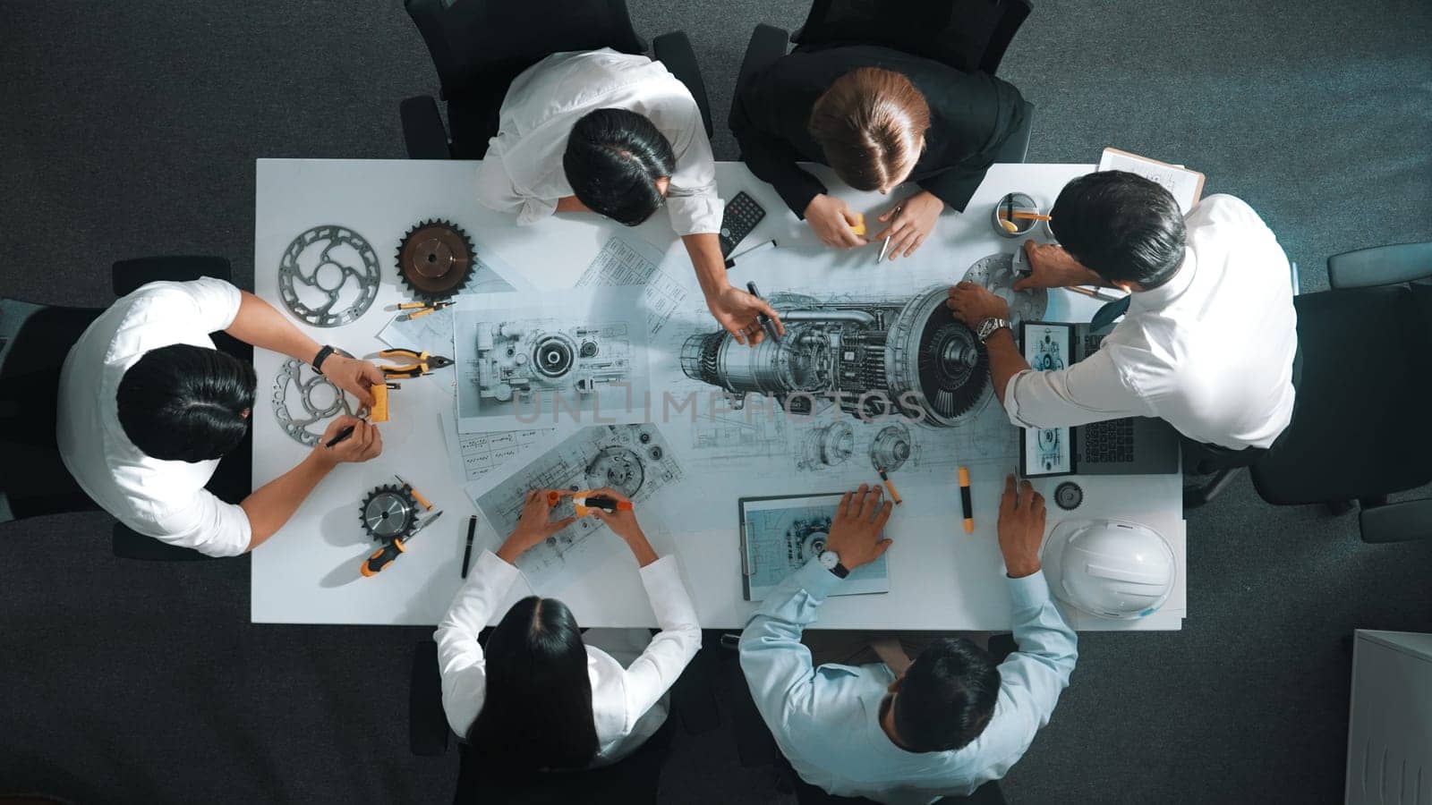 Top down aerial view of smart engineer team working together to design turbine engine. Professional technician discussing about jet engine construction while pointing at part of engine. Alimentation.
