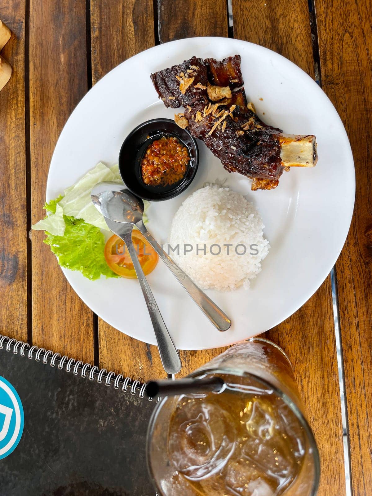 Spicy hot honey roasted grilled spare ribs served with hot chili paste on wooden table and rice also ice tea served in white plate