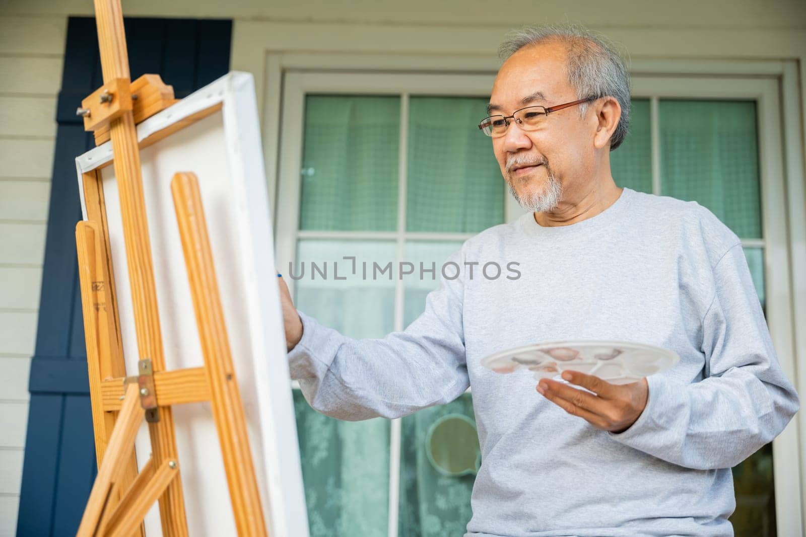 Artist. Asian senior old man painting picture using brush and oil color on canvas, lifestyle elderly people smile paint at his easel, Happy retirement and activity concept