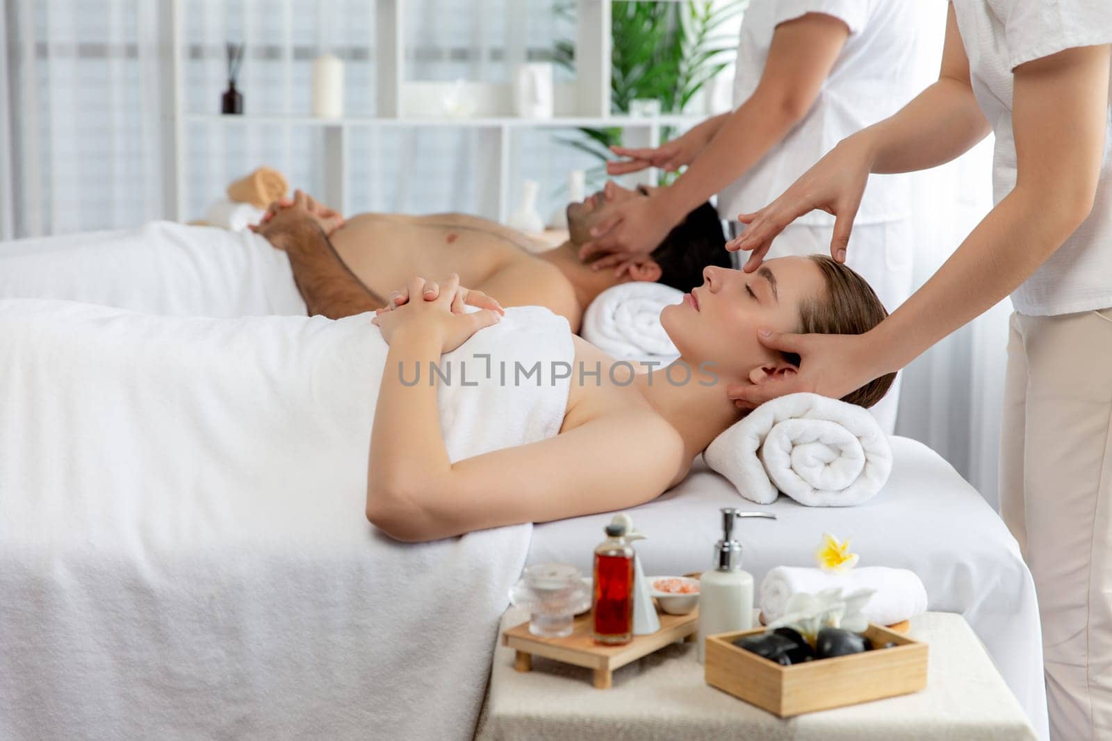 Caucasian couple enjoying relaxing anti-stress head massage and pampering facial beauty skin recreation leisure in dayspa modern light ambient at luxury resort or hotel spa salon. Quiescent