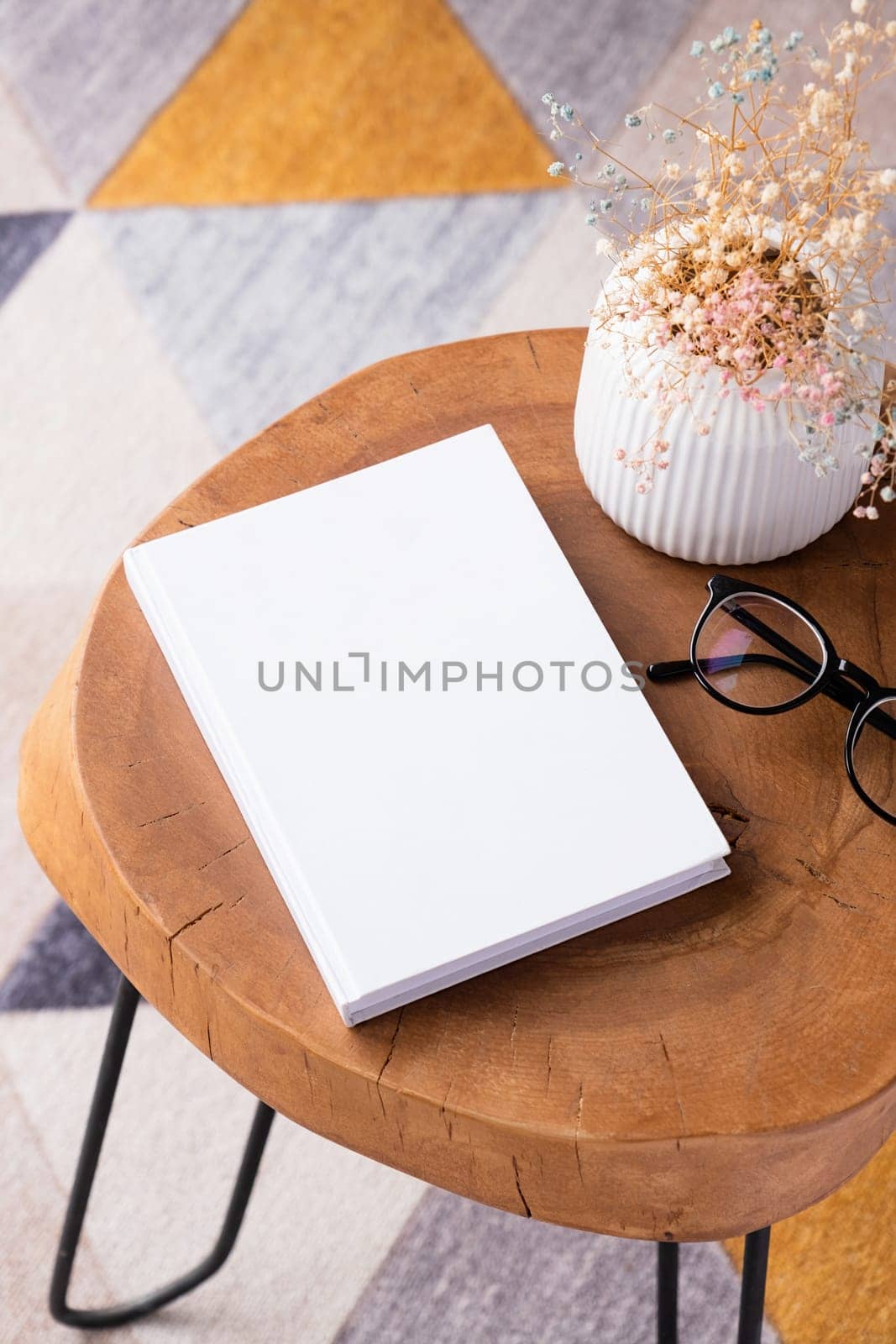 blank book mockup on coffee table with decoration flowers and colorful rug by Desperada