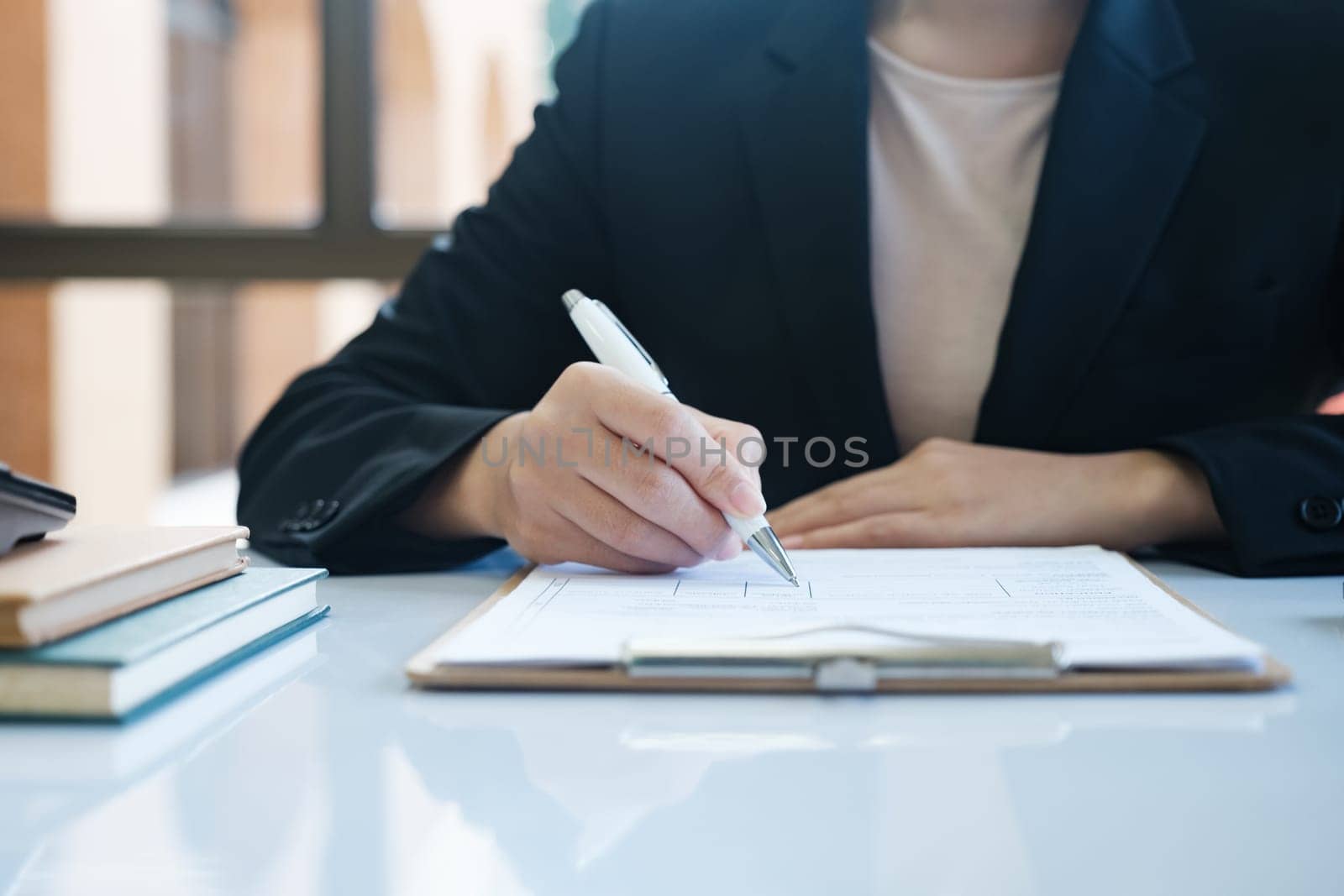 A woman in a suit is writing with a pen on a piece of paper. Concept of professionalism and focus, as the woman is likely working on a task or document