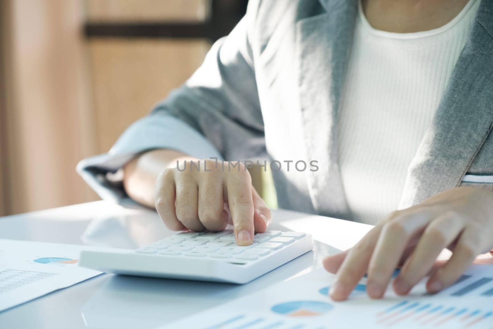 A woman is sitting at a desk with a calculator and a stack of papers. She is focused on her work, possibly working on financial or business-related tasks. Concept of concentration and productivity