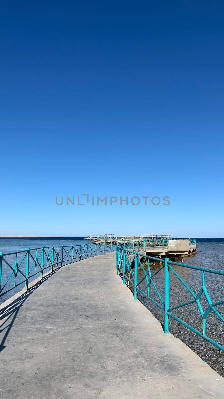 Vertical photo of pier for walk by the sea against the backdrop of clear blue sky on hot summer day
