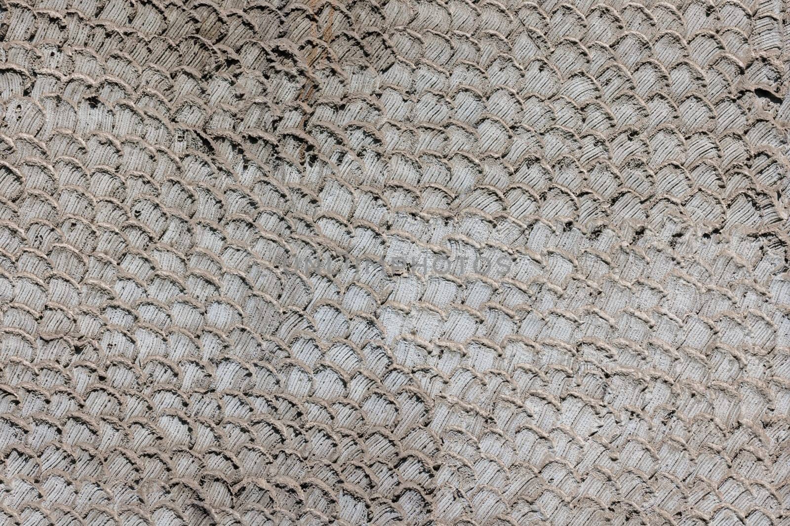Texture of grey snakeskin or fish scale pattern finish on gray concrete wall, full-frame background.