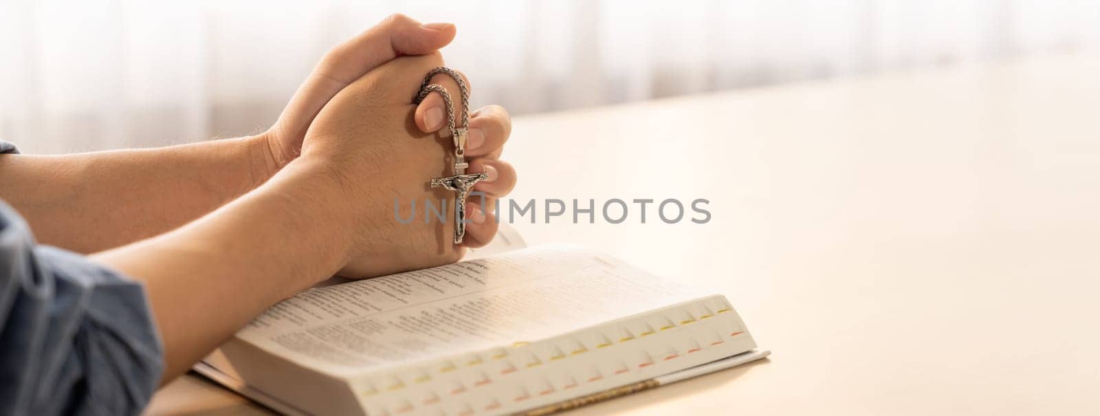 Asian male folded hand prayed on holy bible book while holding up a pendant crucifix. Spiritual, religion, faith, worship, christian and blessing of god concept. Blurring background. Burgeoning.