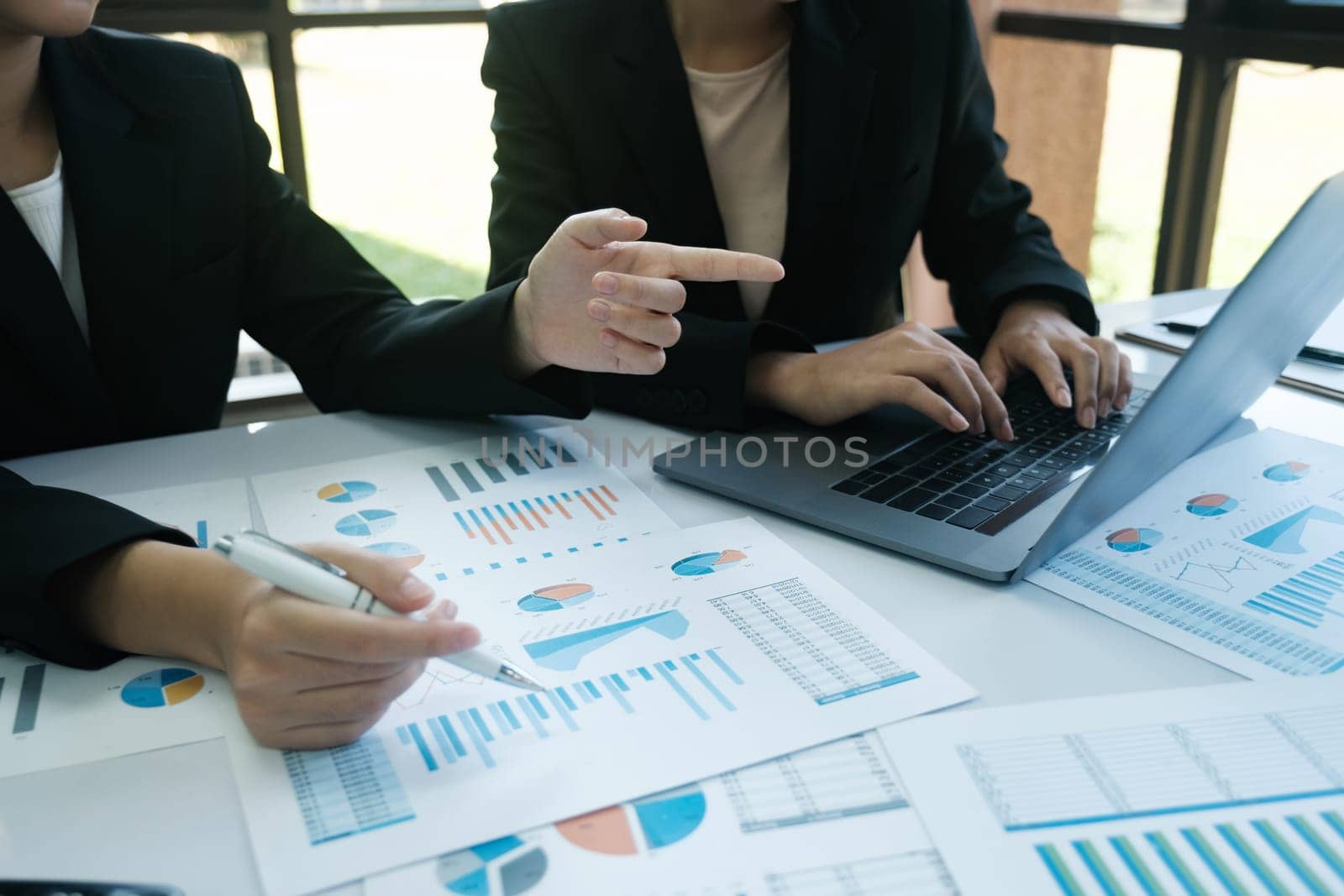 Two women are working on a project together, one pointing at a graph on a table by ijeab