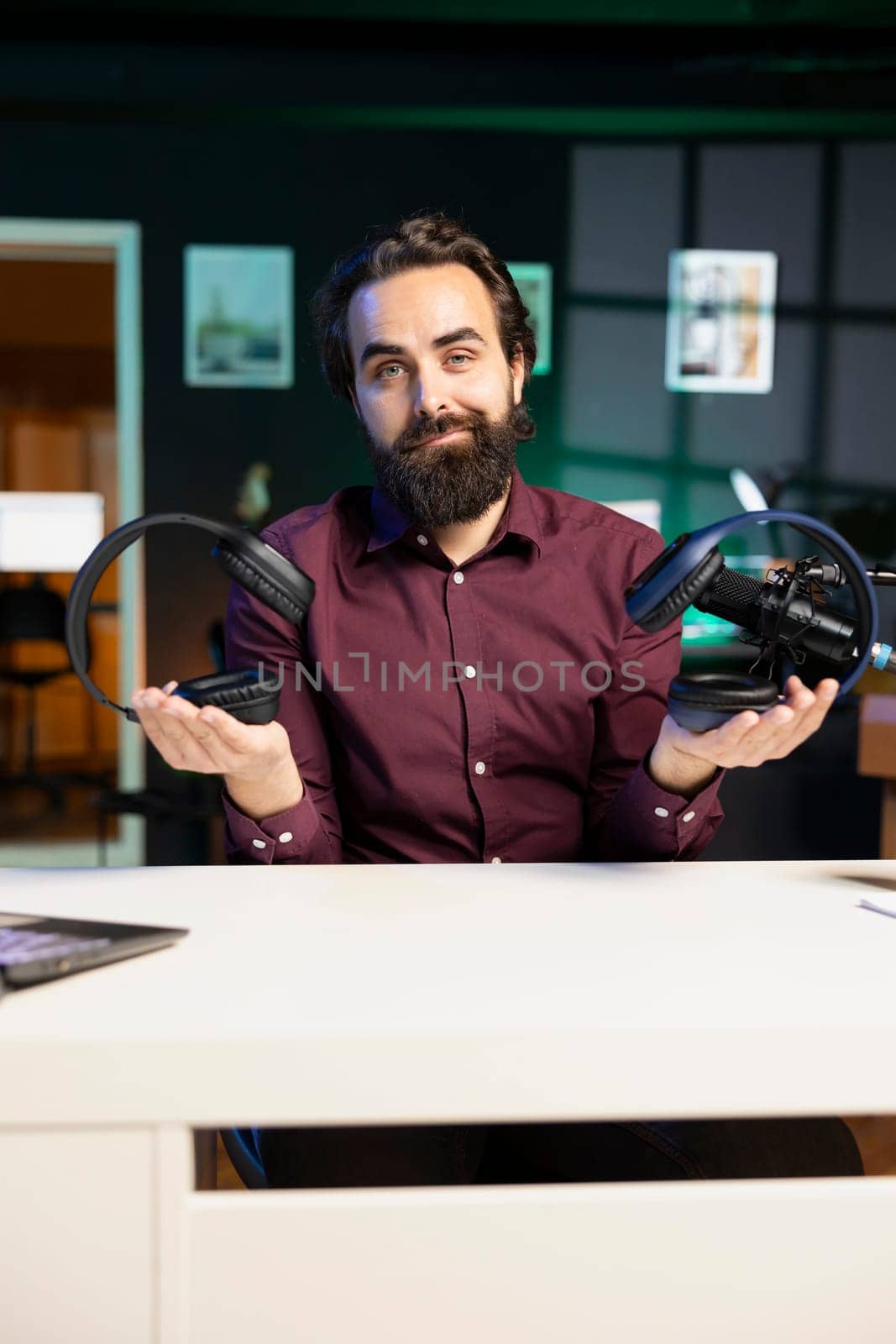 Content creator in neon lit home studio filming wireless headphones review for online streaming platforms. Media star hosts internet show, comparing music listening devices from different price ranges