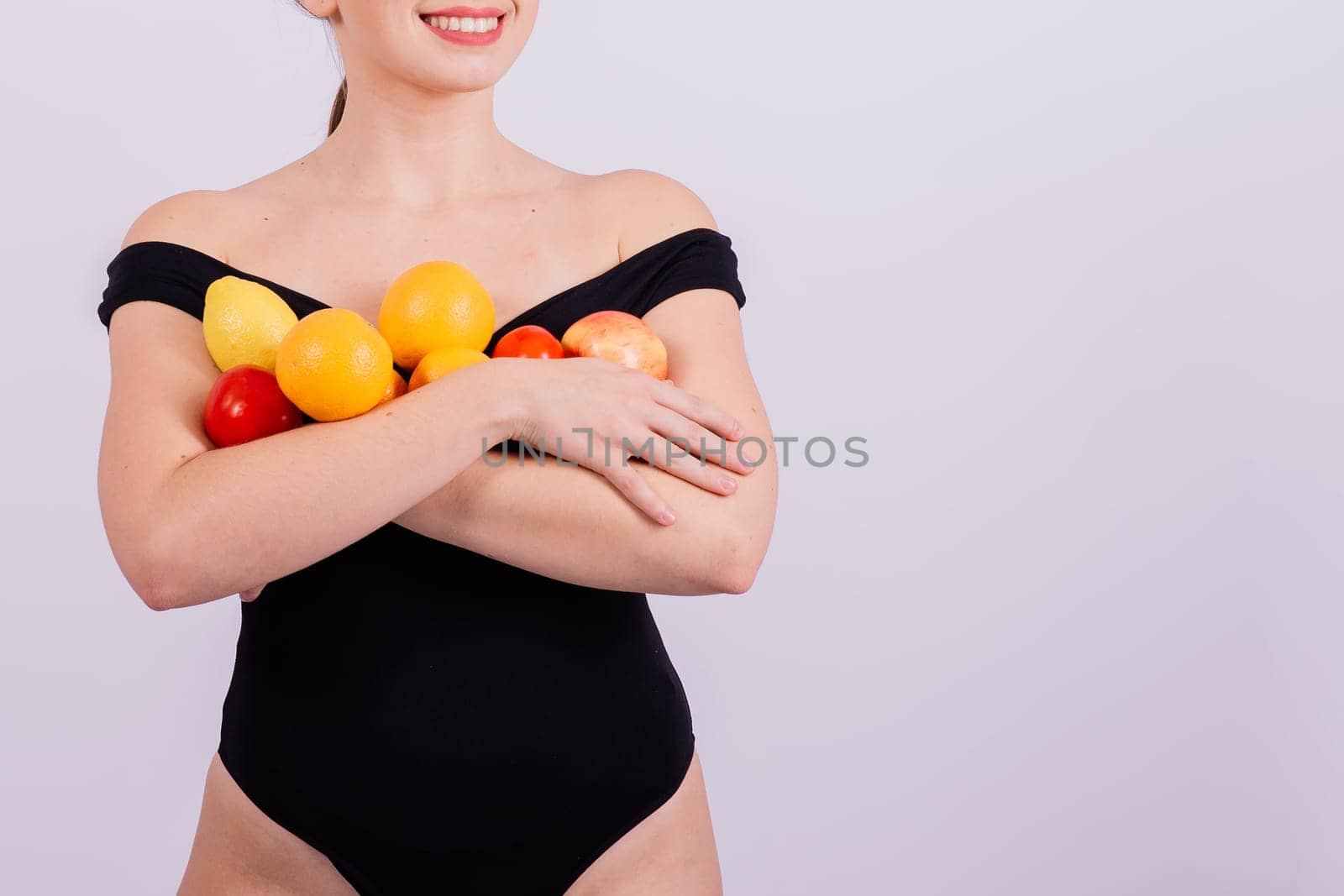 A female holding apples, lemons, oranges in different arms isolated on grey background. by Zelenin