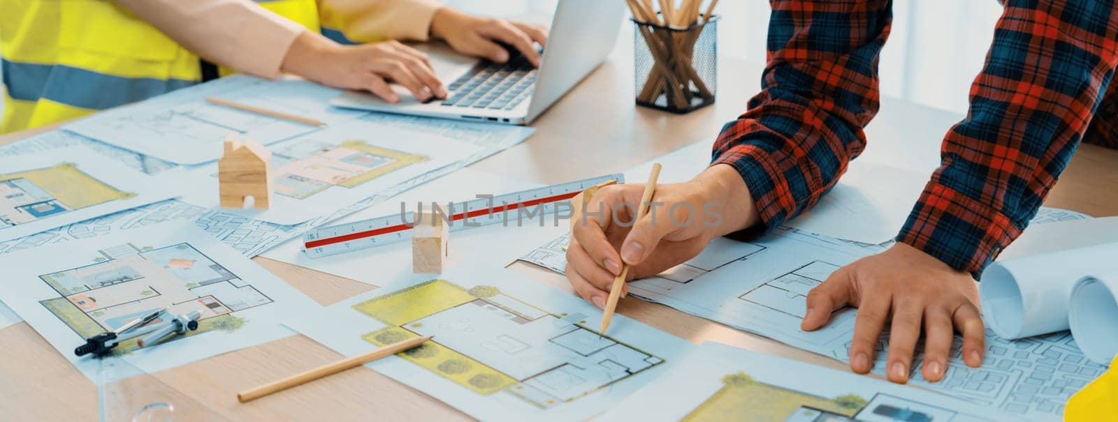 A cropped portrait of professional architect working with blueprint during safety engineer using laptop analysis data at meeting table with document scatter around. Close up. Delineation.