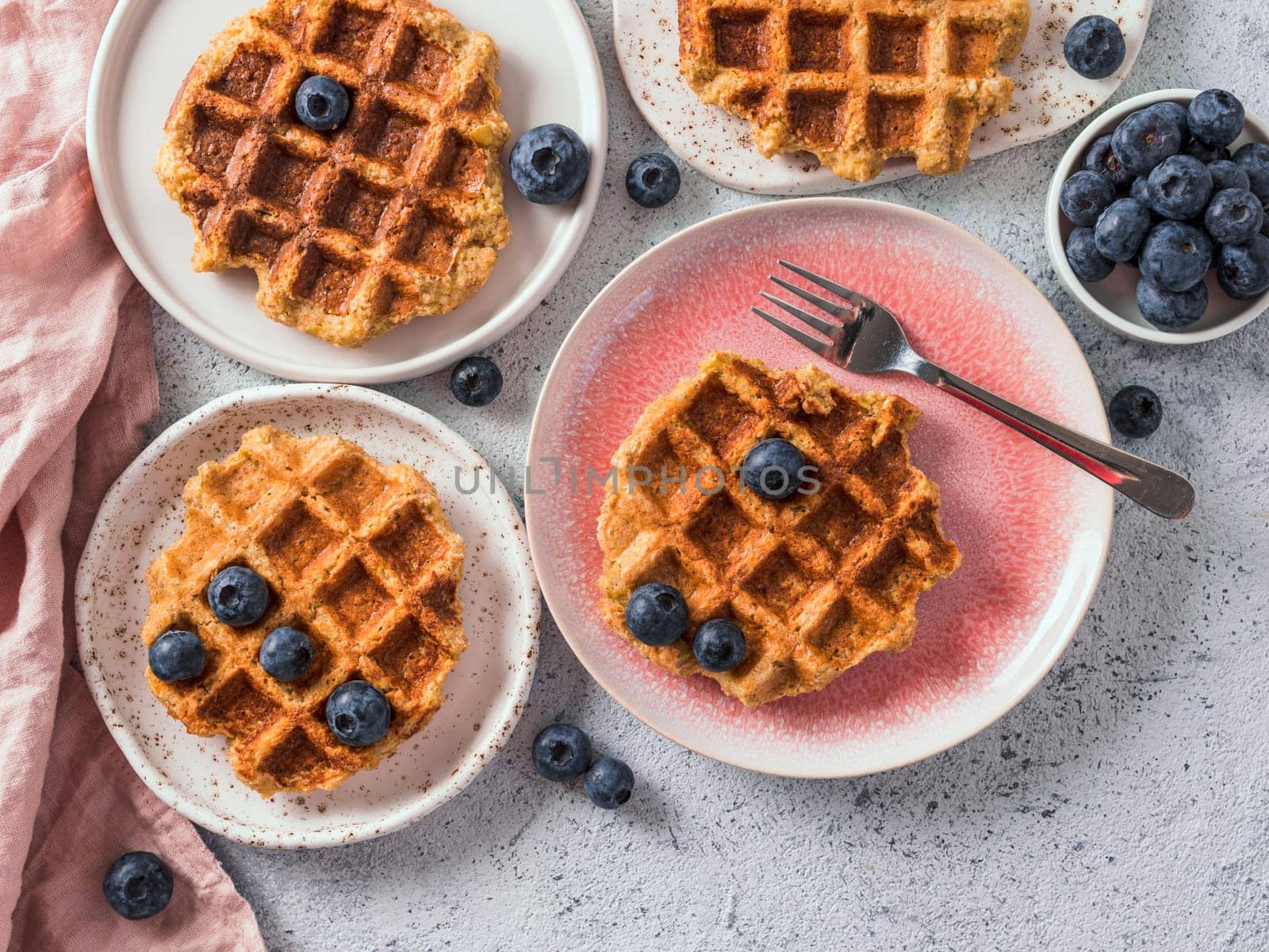Easy healthy gluten free oat waffles with copy space. Plates with appetizing homemade waffles with oat flour decorated blueberries, on light gray cement background. Top down view or flat lay