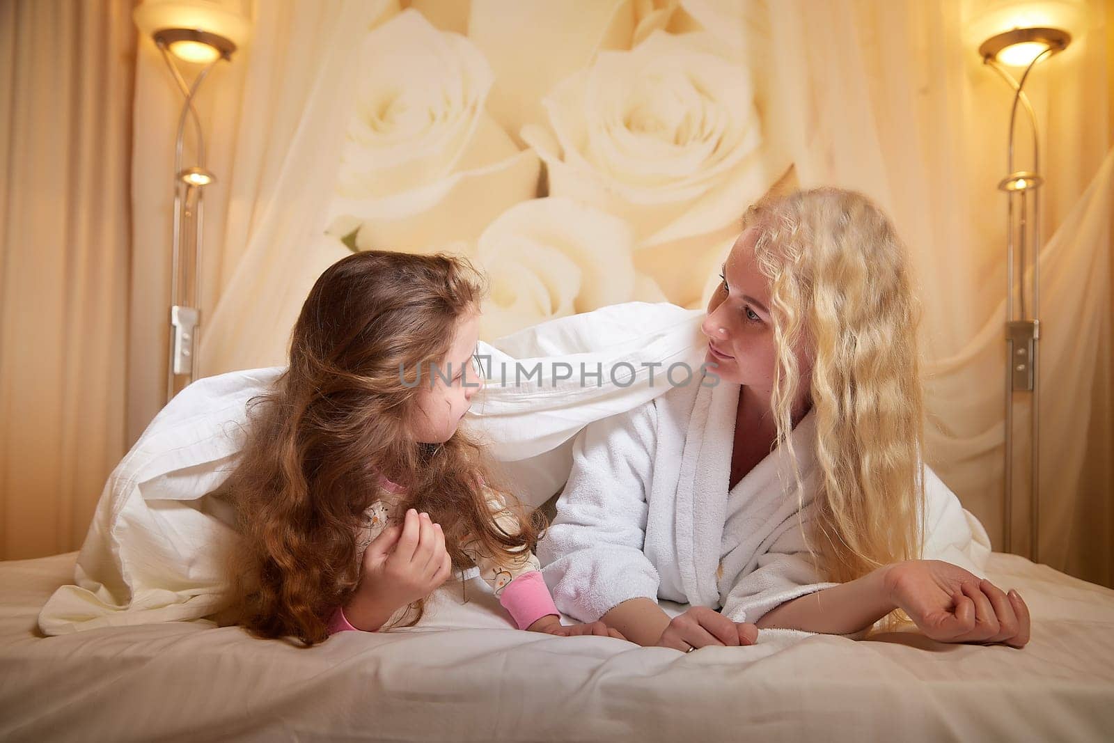 Mother and daughter happily relax and fun together on bed in bedroom. The concept of tenderness between mom and girl