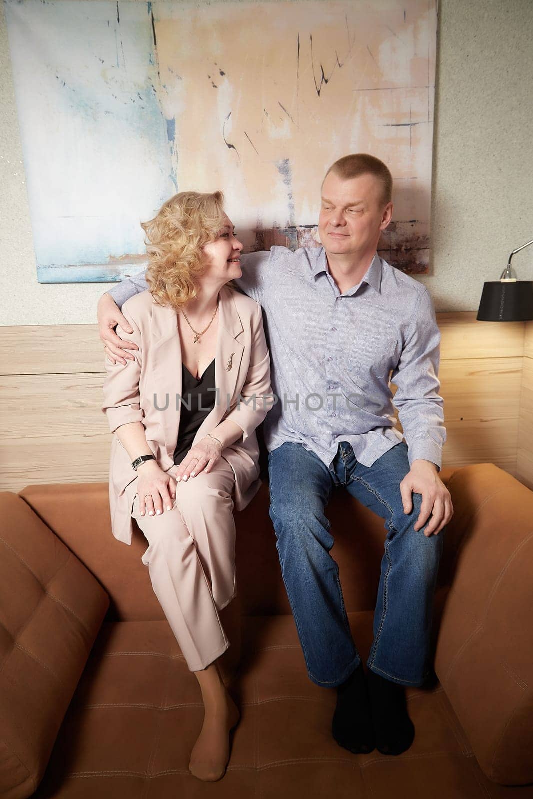 Loving adult couple communicates and embraces privately in the living room or in hotel. Woman is wearing business formal suit and man is wearing jeans and a shirt, indicating a close relationship