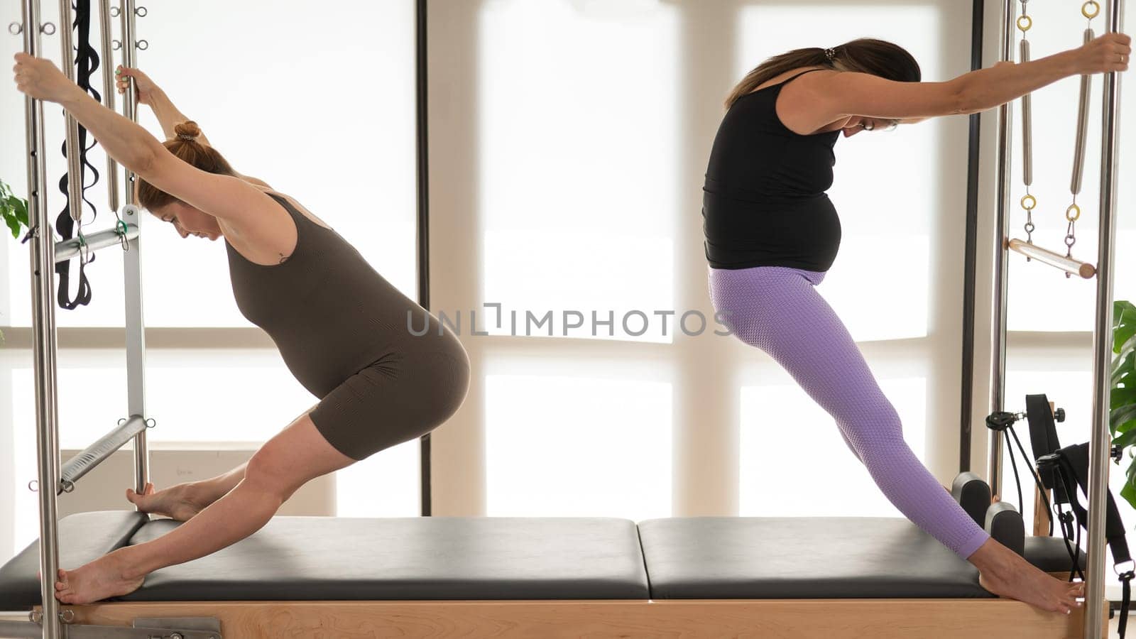 Two pregnant women are doing Pilates on a Cadillac reformer