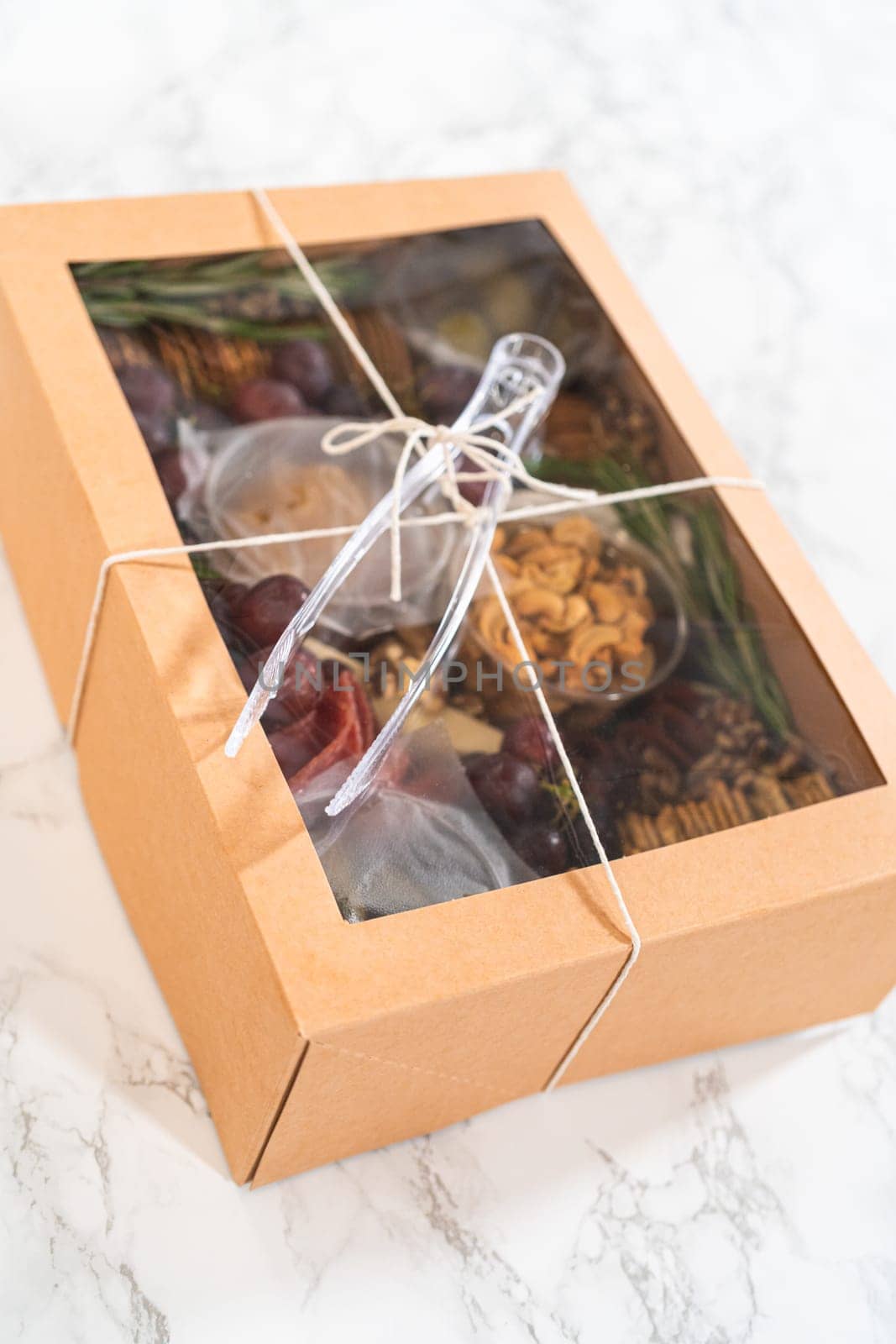 Charcuterie box featuring sliced meat, cheese, crackers, and grapes, all neatly packaged in a brown gifting box.