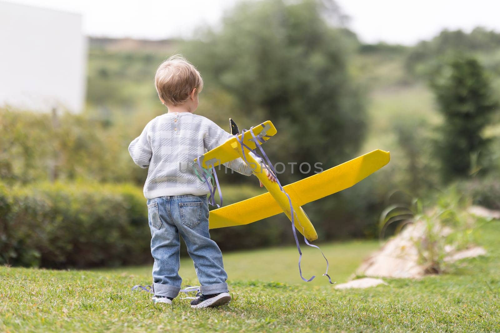 Boy toddler plays with toy airplane in park - telephoto