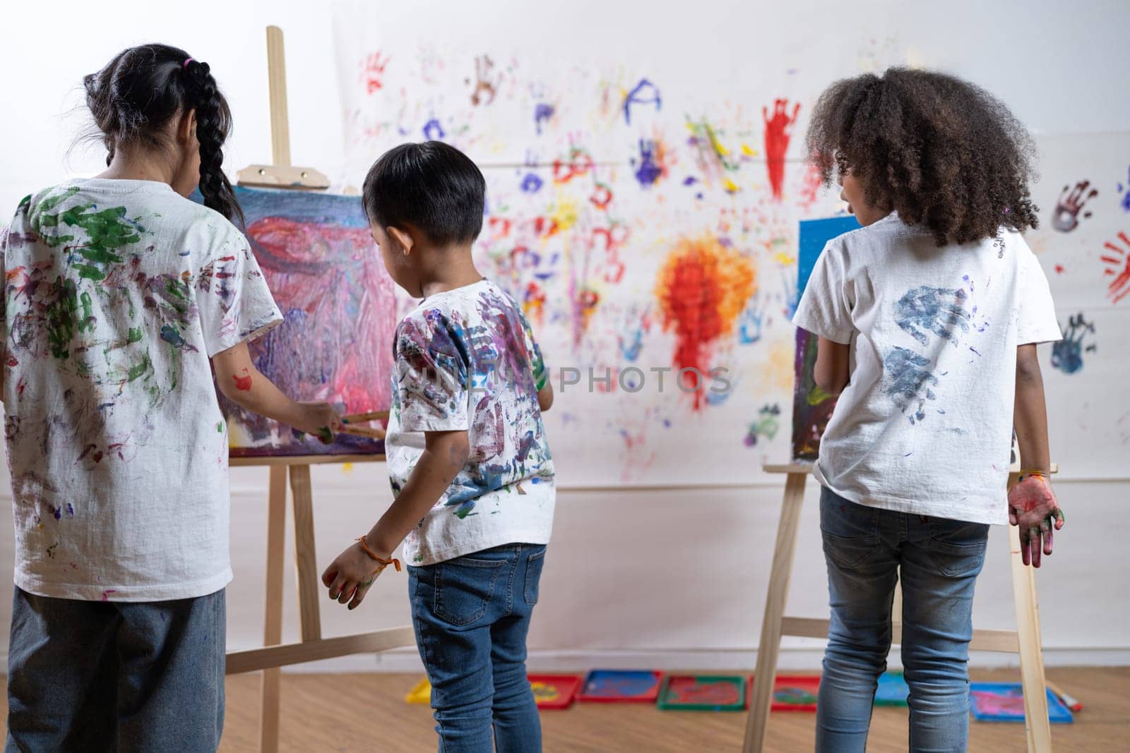 Students painting on canvas show artist skill in drawing class. Kid paint canvas all around use paintbrushes with blue and red as main color. Wall put paper printed with hand of children. Erudition.