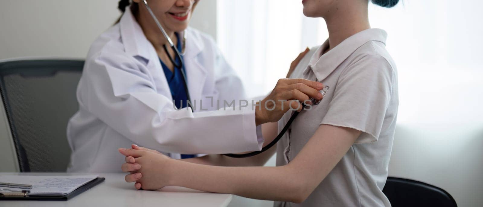 Asian woman elderly doctor at hospital taking care of young woman. Doctor measure heart rate by stethoscope on older patient. Medical insurance service concept by nateemee