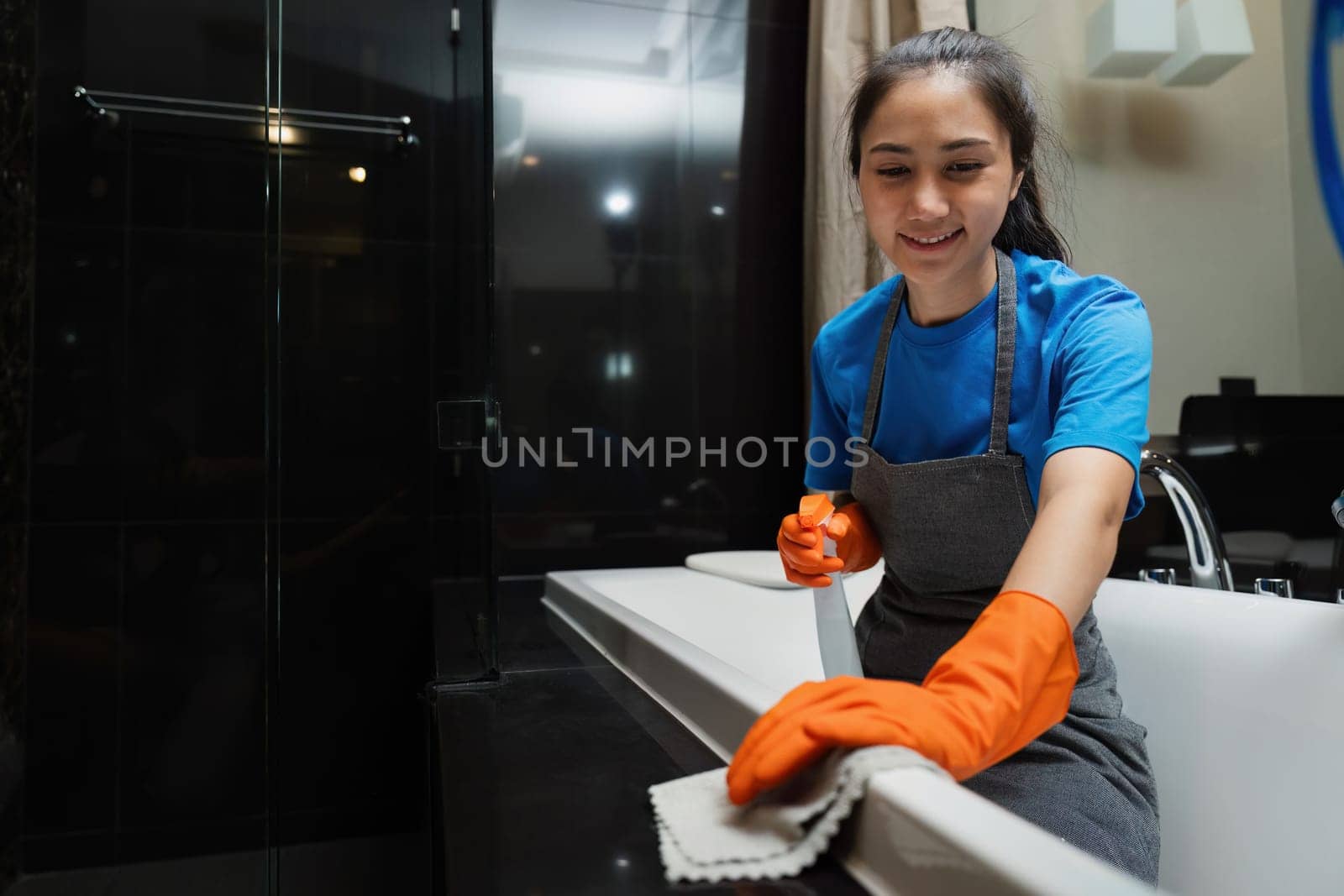 Cleaning online service. yong woman housekeeper cleaning bathtub in bathroom with a cloth. House cleaning service concept by itchaznong