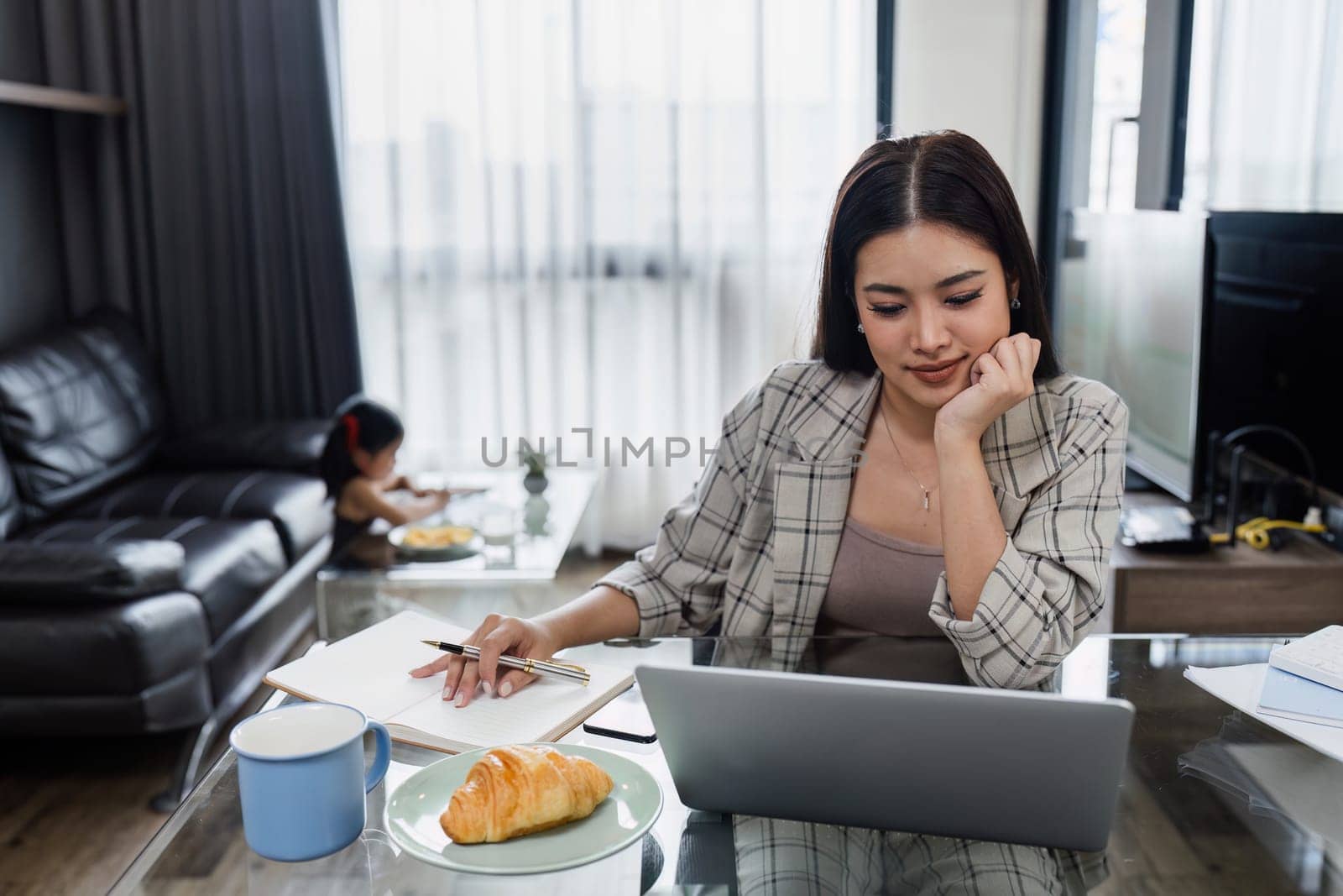 Business woman working from home and taking care of child while working, child doing activities in the background.
