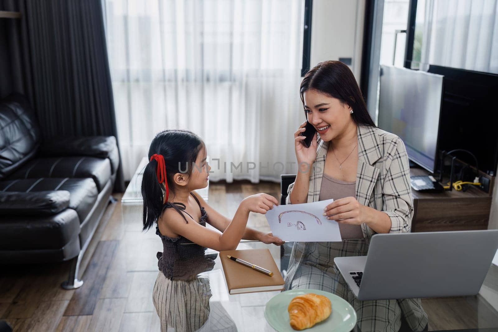 business woman work from home and take care of her child while working, doing activities with her child while talking on mobile.