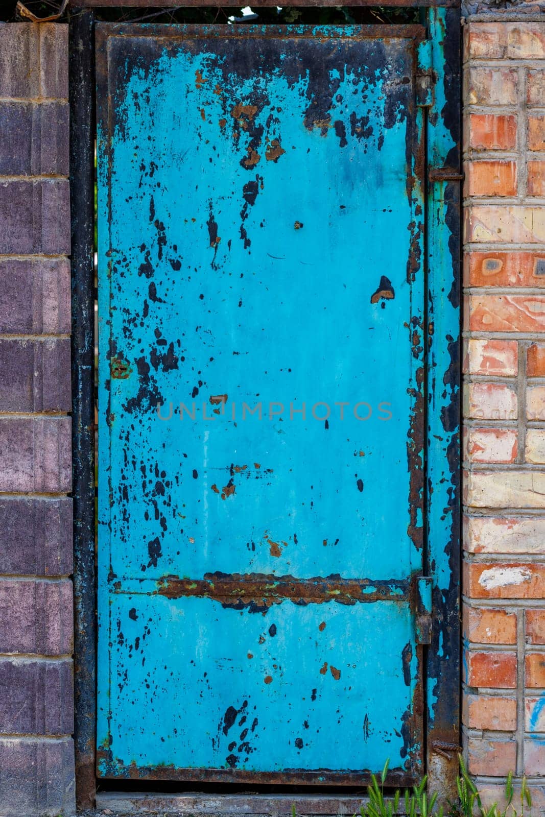 A blue steel door in a brick wall or fence, peeled off paint