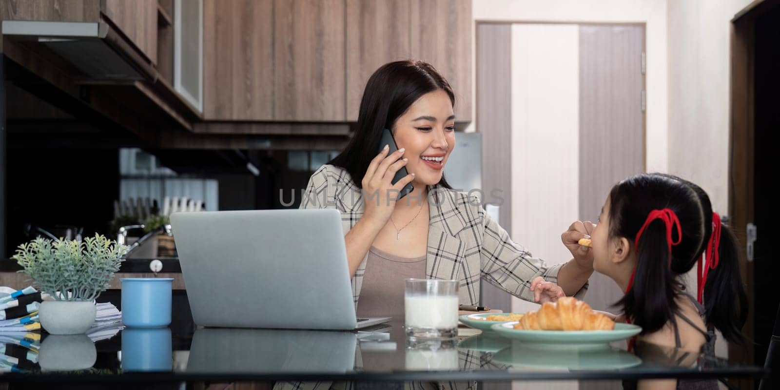 Working mom work from home office. Happy mother and daughter feed snacks to each other. businesswoman and cute child using laptop work freelancer workplace in home, Lifestyle family moment.