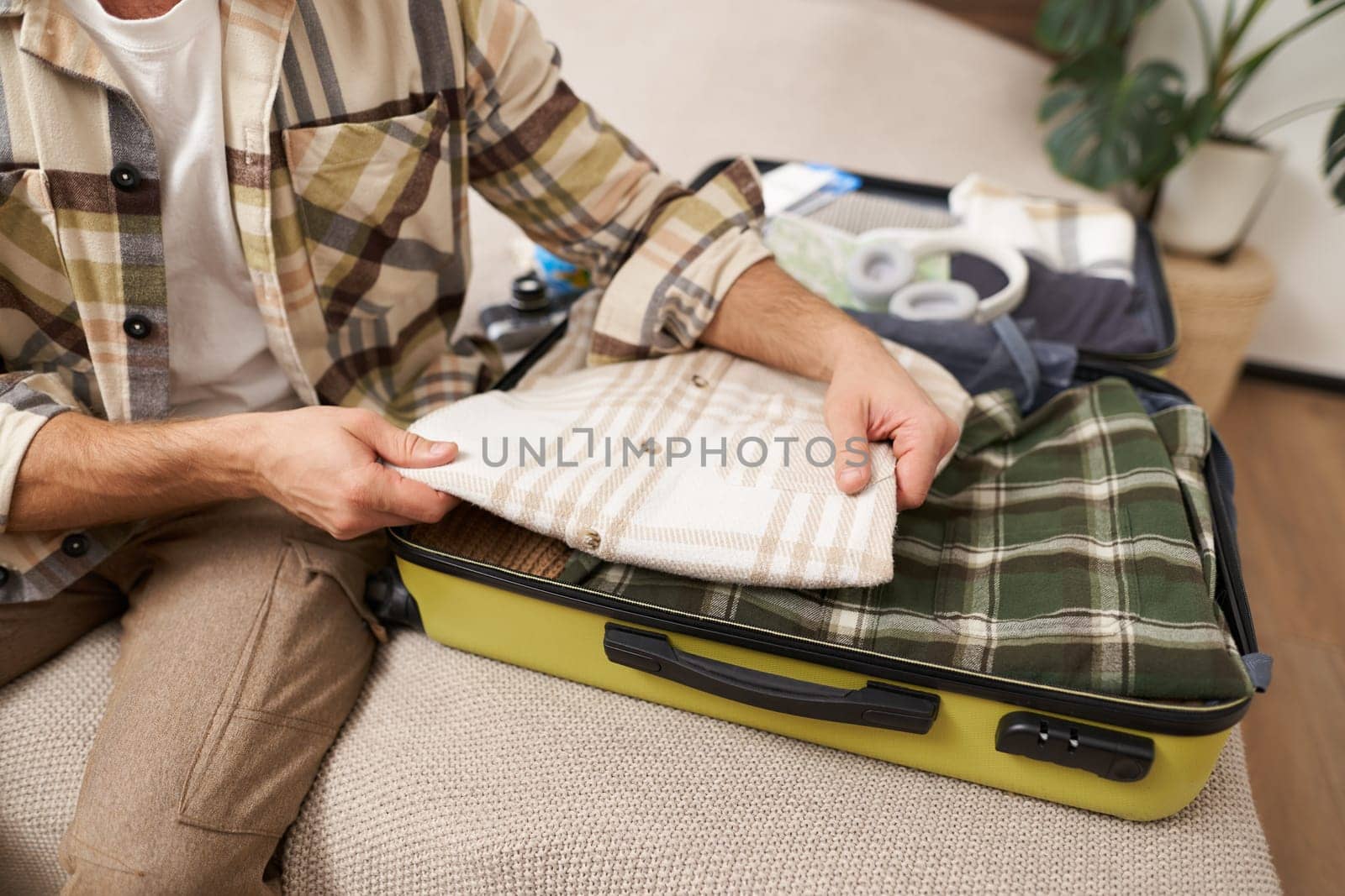 Cropped shot of male hands putting clothes inside suitcase, packing for business work trip or going on vacation, getting ready for holiday journey, preparing luggage.