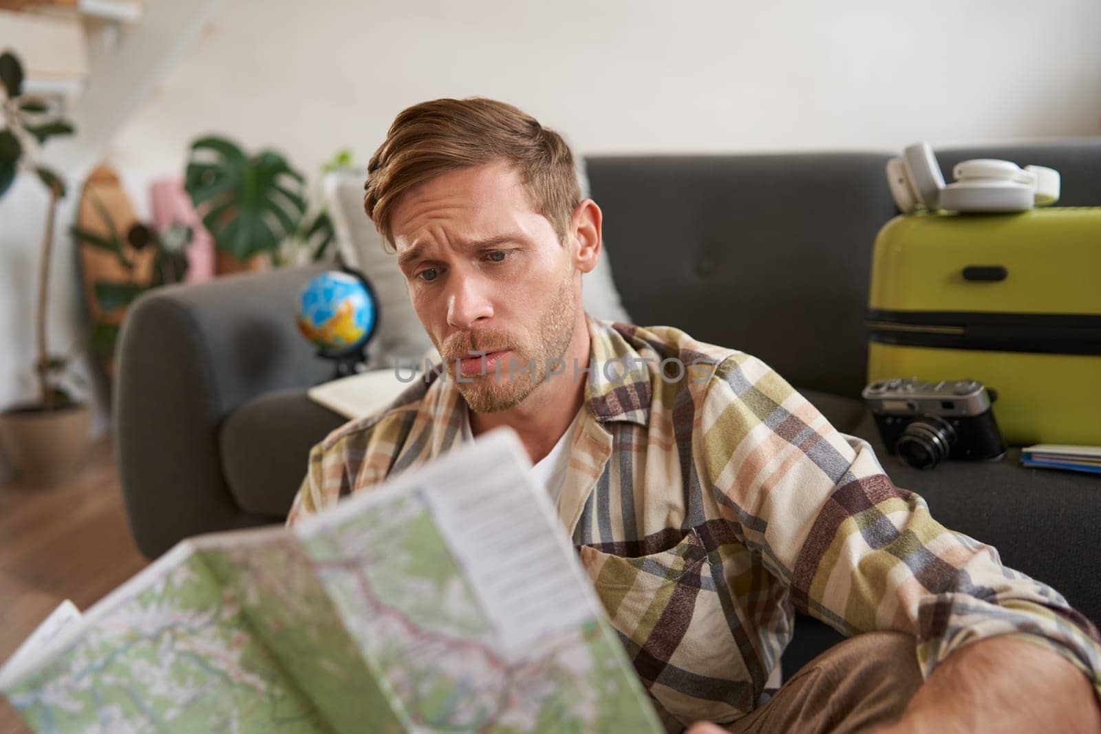 Portrait of confused guy looking at travel map, choosing route, going on holiday, plans to go on vacation by Benzoix