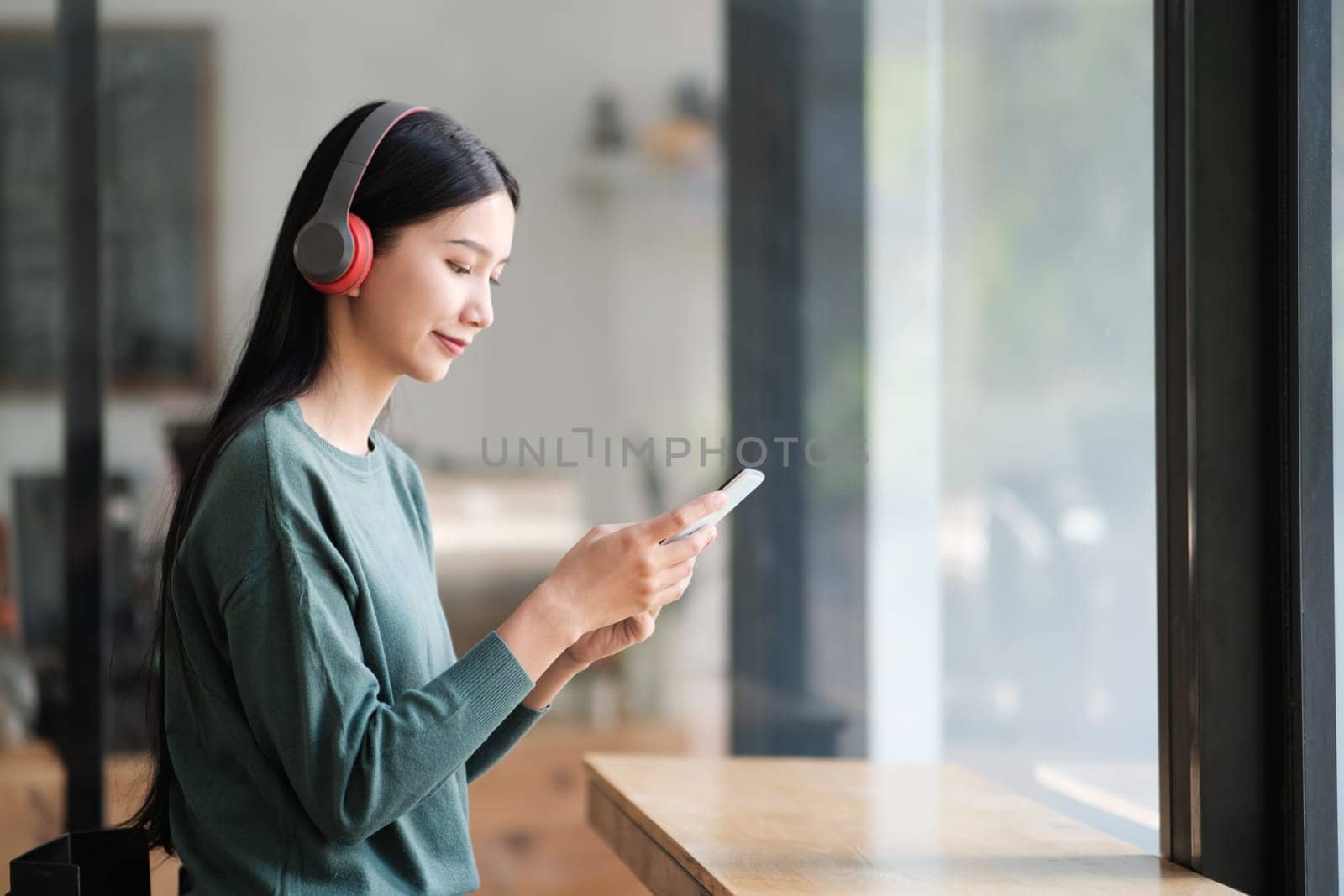 A woman is sitting at a table with a cell phone in her hand. She is wearing headphones and she is listening to music